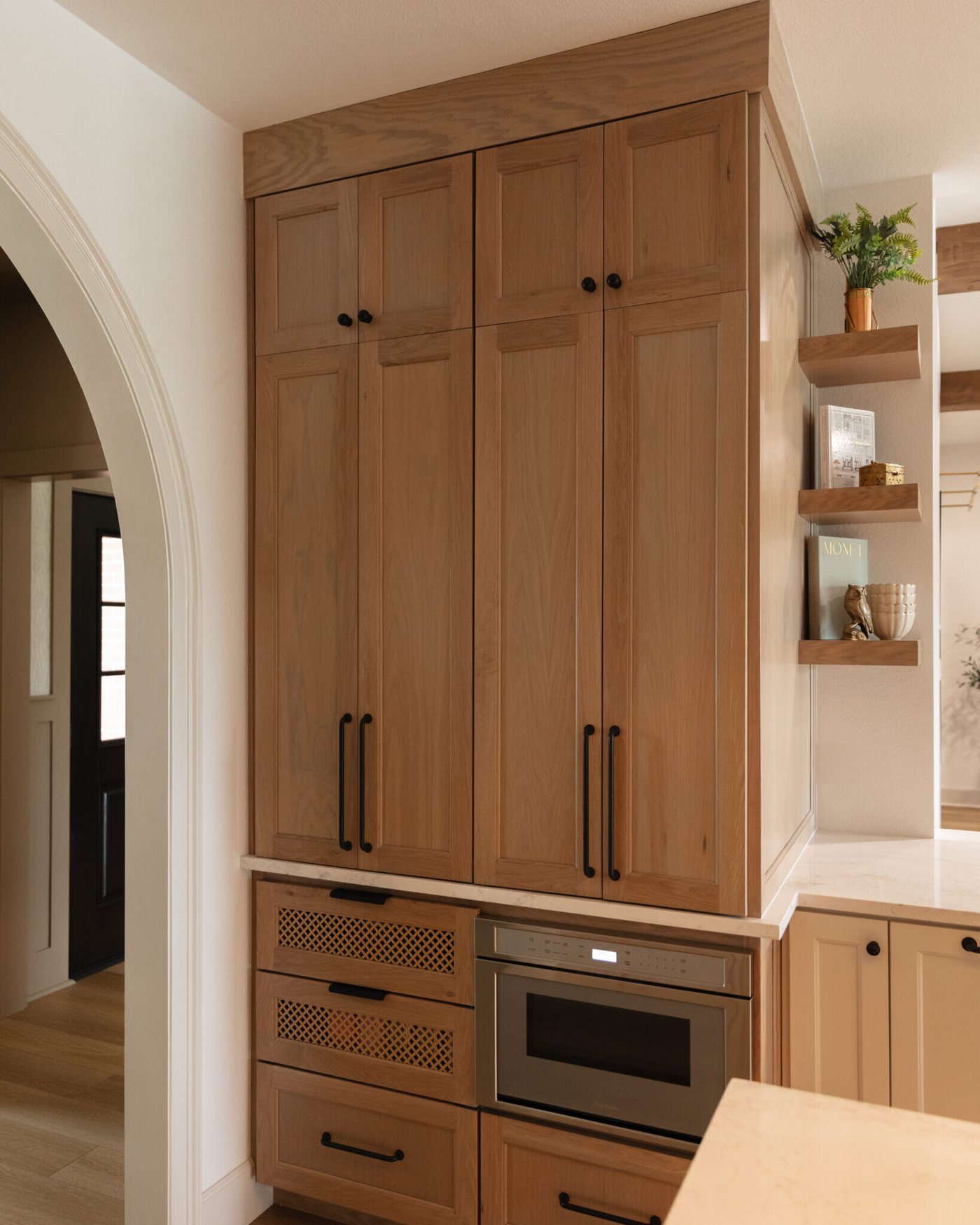 Floor to ceiling white oak pantry doors beside a built-in oven and microwave in the Alexandria project by Jennifer Kizzee Design