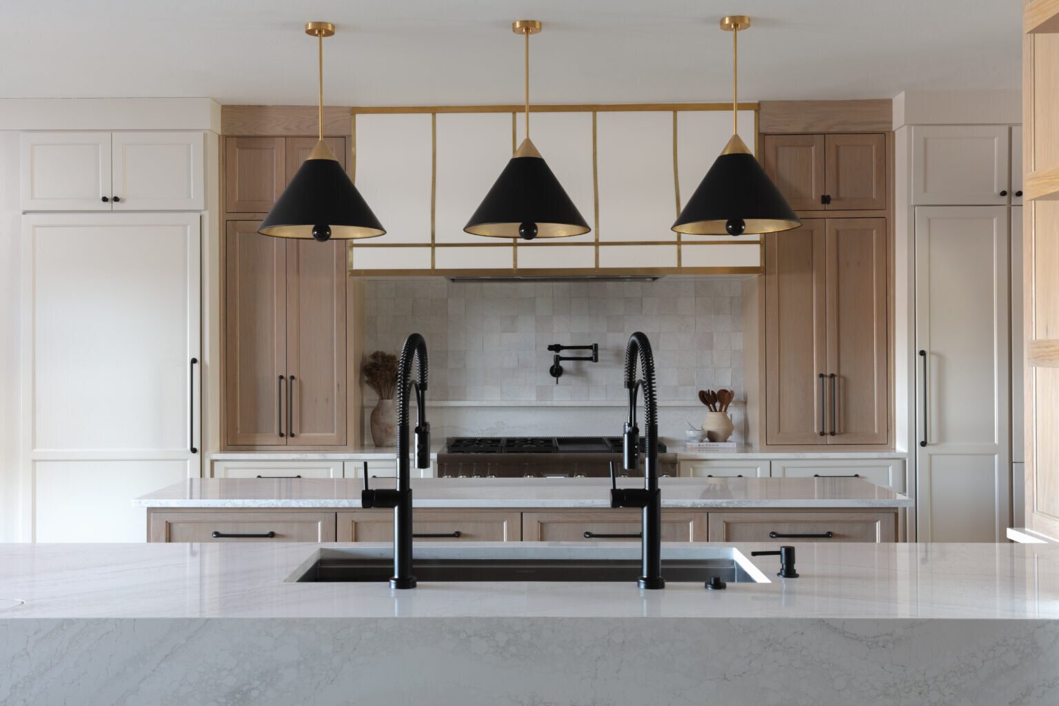 Kitchen island in marble under black cone pendants on a brass frame in the Alexandria project by Jennifer Kizzee Design