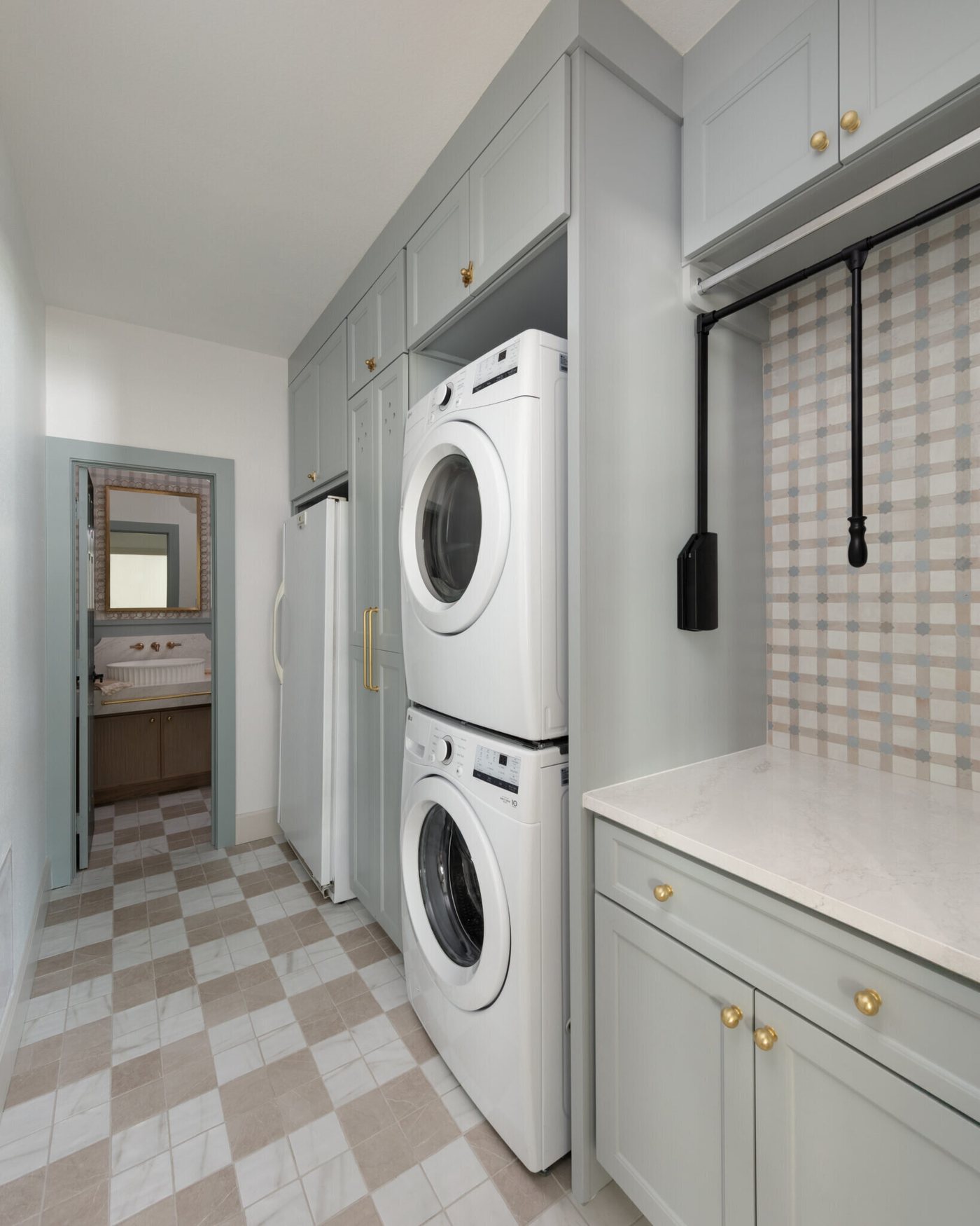 Laundry room in sage green cabinetry with a stacked washer and dryer over a checkerboard tile floor in the Alexandria project by Jennifer Kizzee Design
