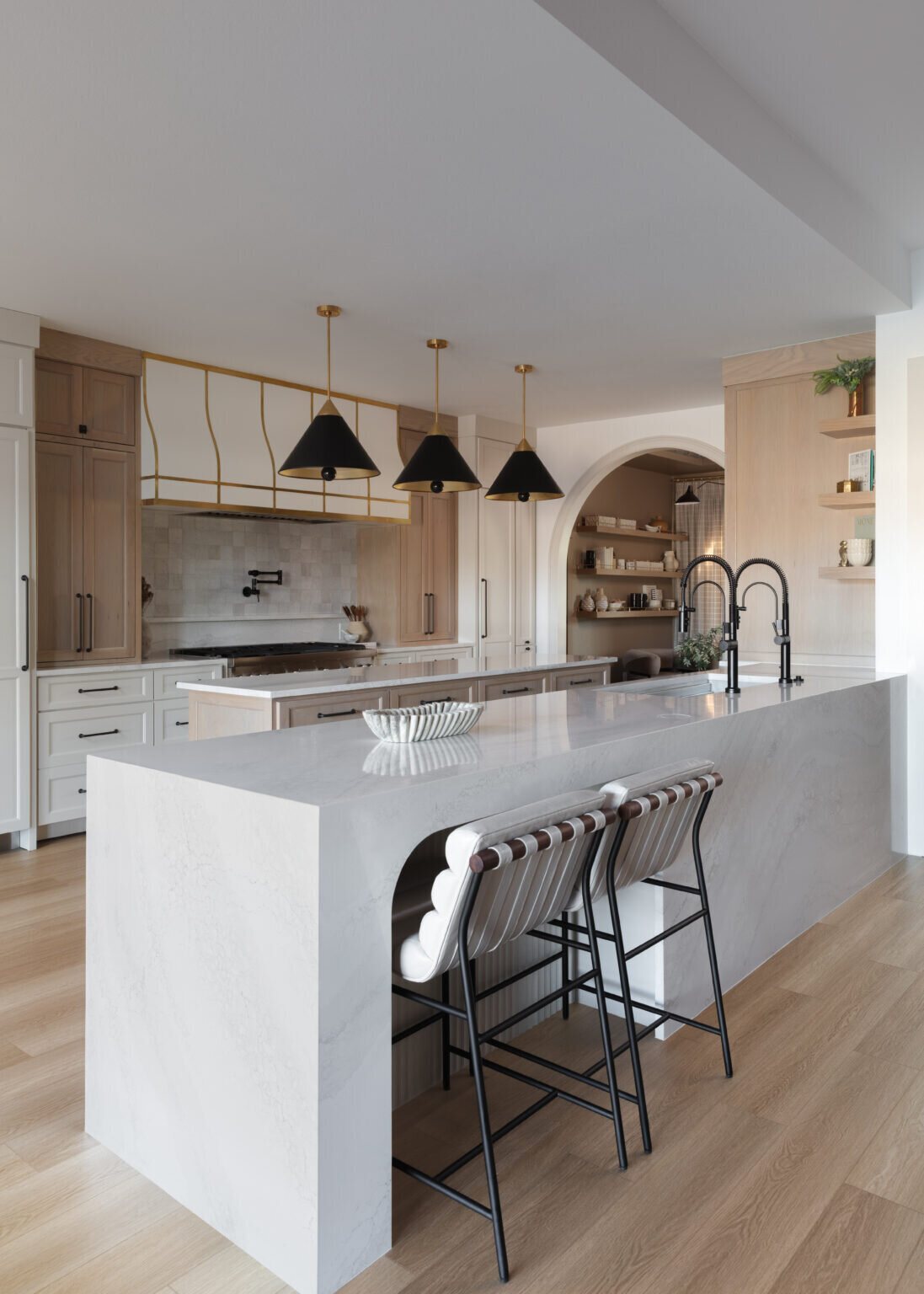 Marble waterfall island with woven counter stools under black cone pendants in the Alexandria project by Jennifer Kizzee Design