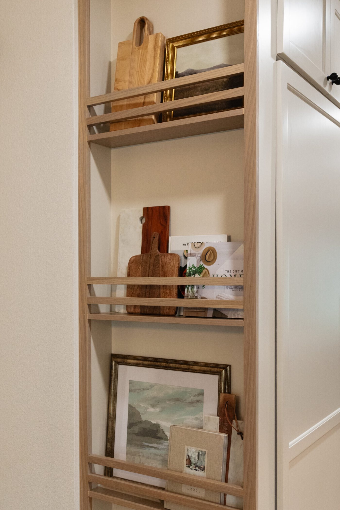 Pantry with brass rail shelves holding boards, framed art and ceramics in the Alexandria project by Jennifer Kizzee Design
