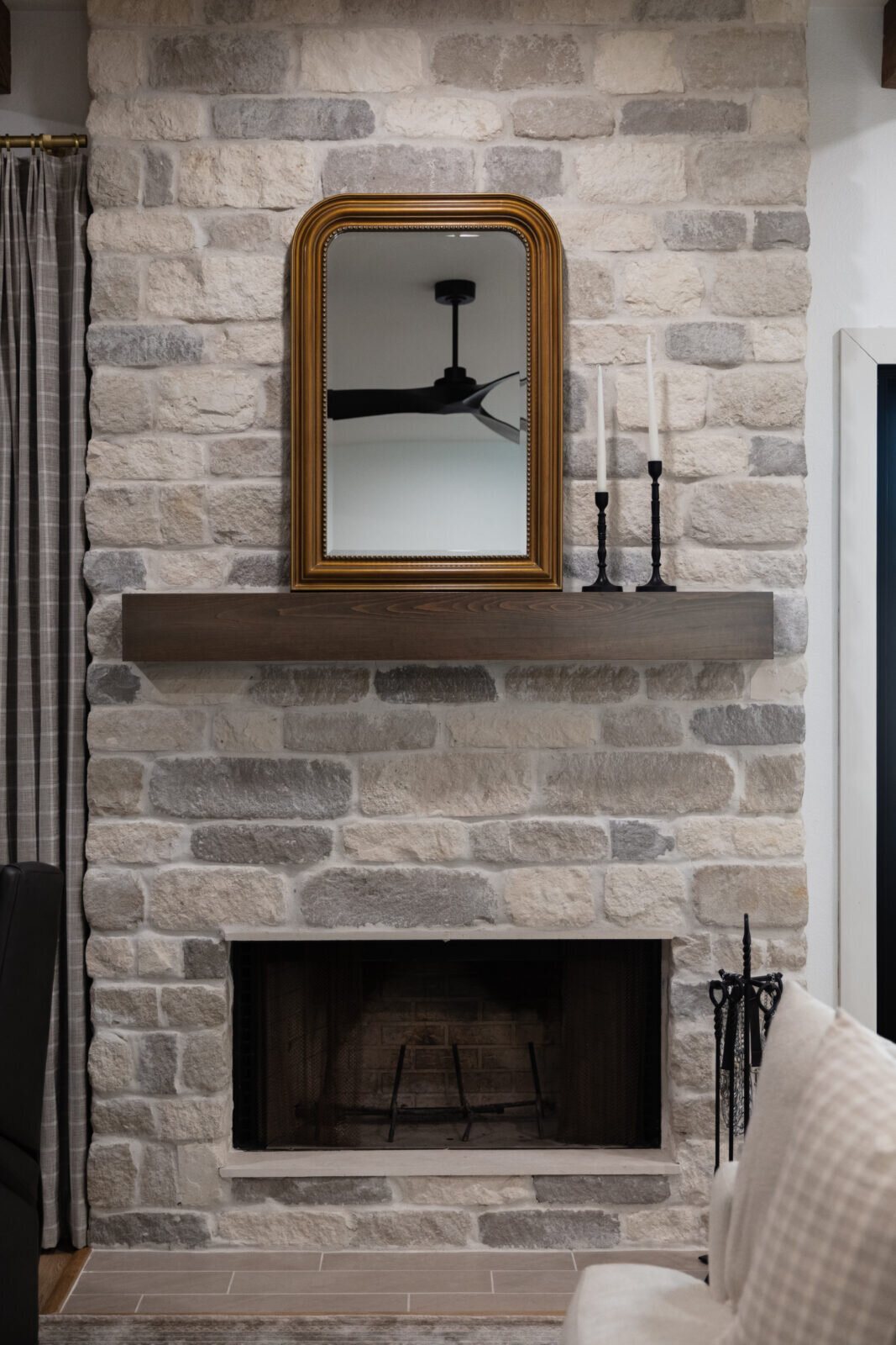 Stone fireplace with a wood mantel and a gilt arched mirror above it in the Alexandria project by Jennifer Kizzee Design