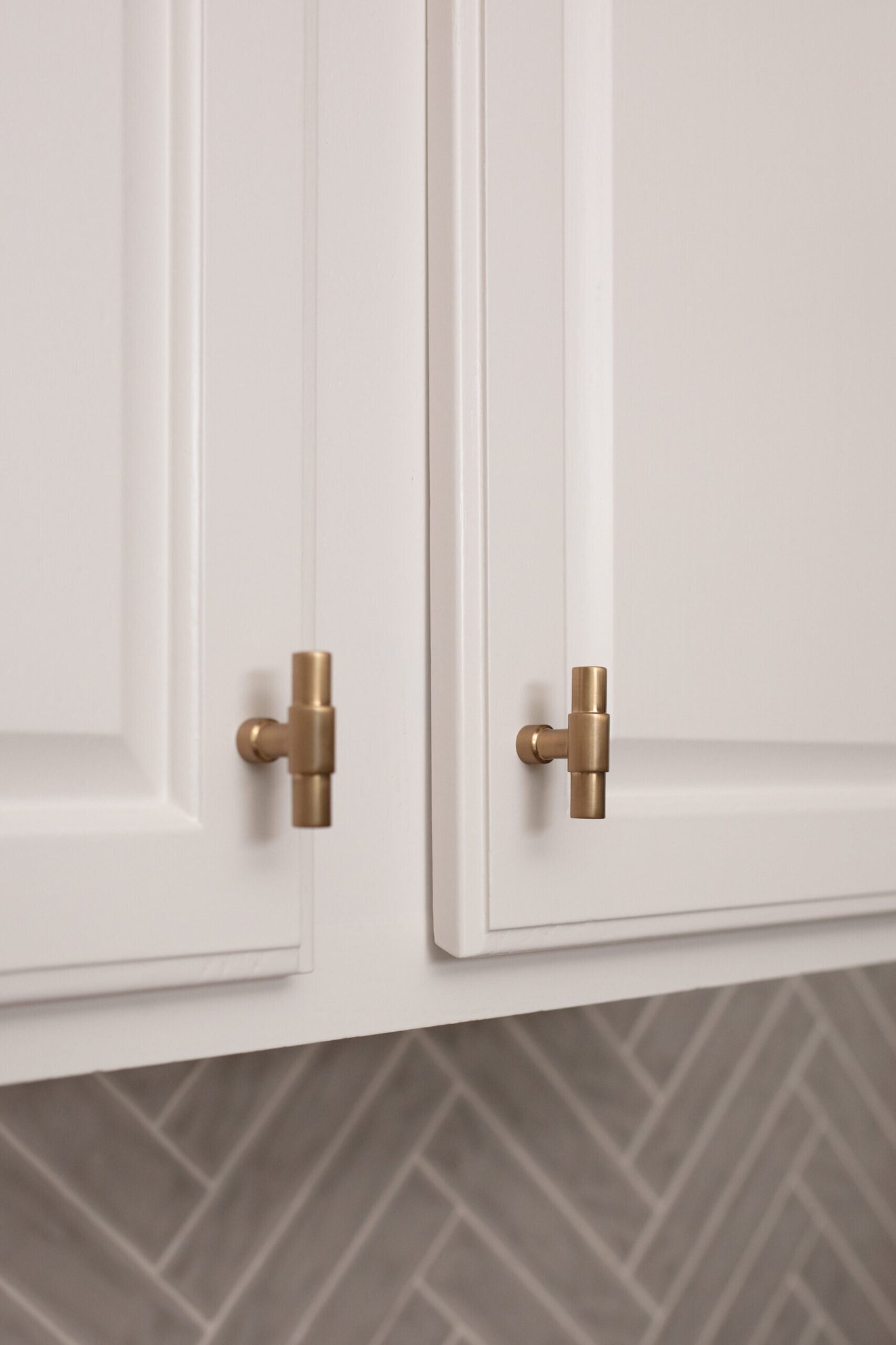 Brass knobs on white cabinet doors above a gray herringbone floor in the Ambrose Kitchen project by Jennifer Kizzee Design