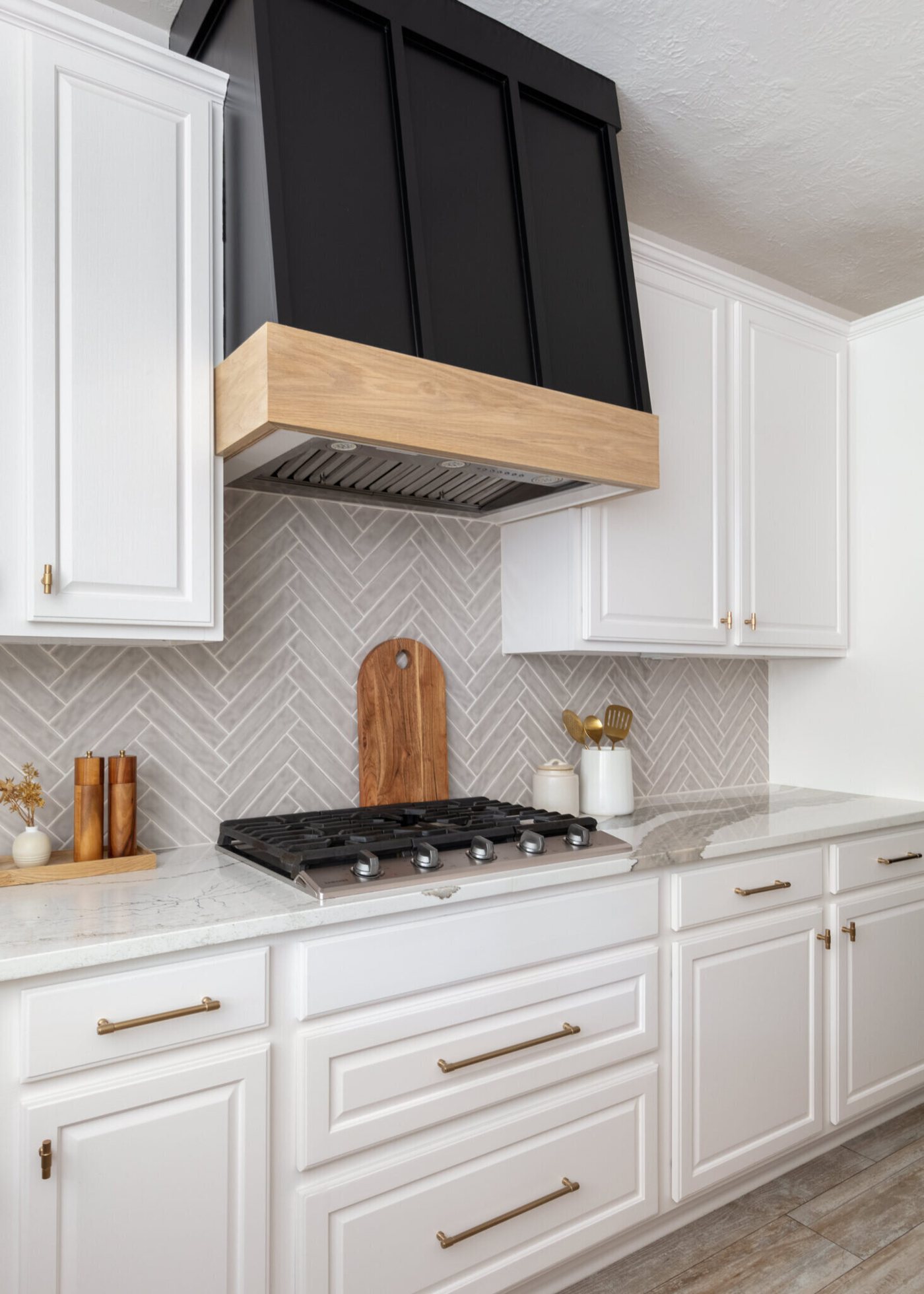 Gas cooktop under a black and wood hood with the herringbone tile behind it in the Ambrose Kitchen project by Jennifer Kizzee Design