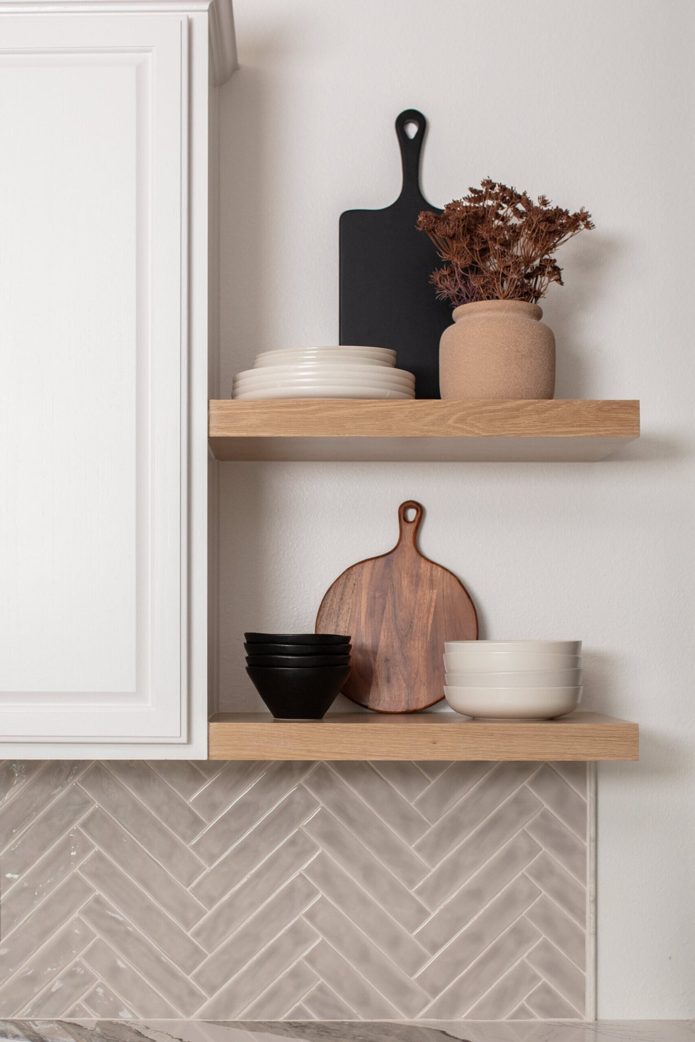 Open white oak shelves against herringbone tile holding boards and bowls in the Ambrose Kitchen project by Jennifer Kizzee Design