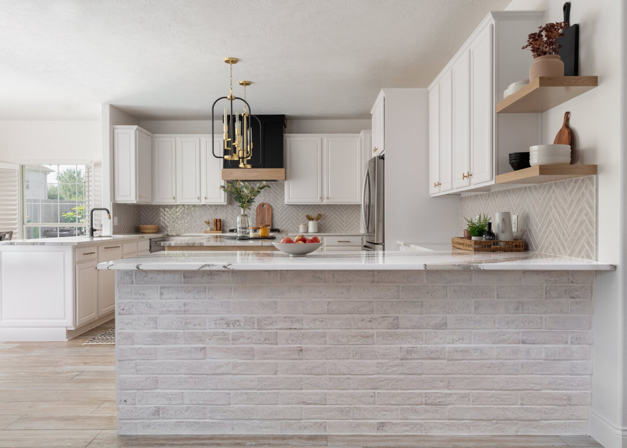 White kitchen with a stacked stone peninsula, a black hood and brass lanterns in the Ambrose Kitchen project by Jennifer Kizzee Design
