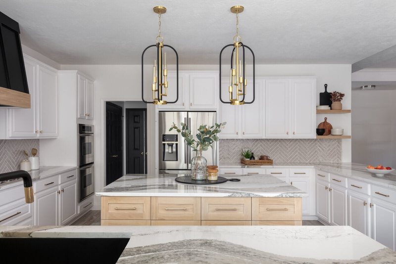 White kitchen with a veined quartz island and brass lantern pendants in the Ambrose Kitchen project by Jennifer Kizzee Design