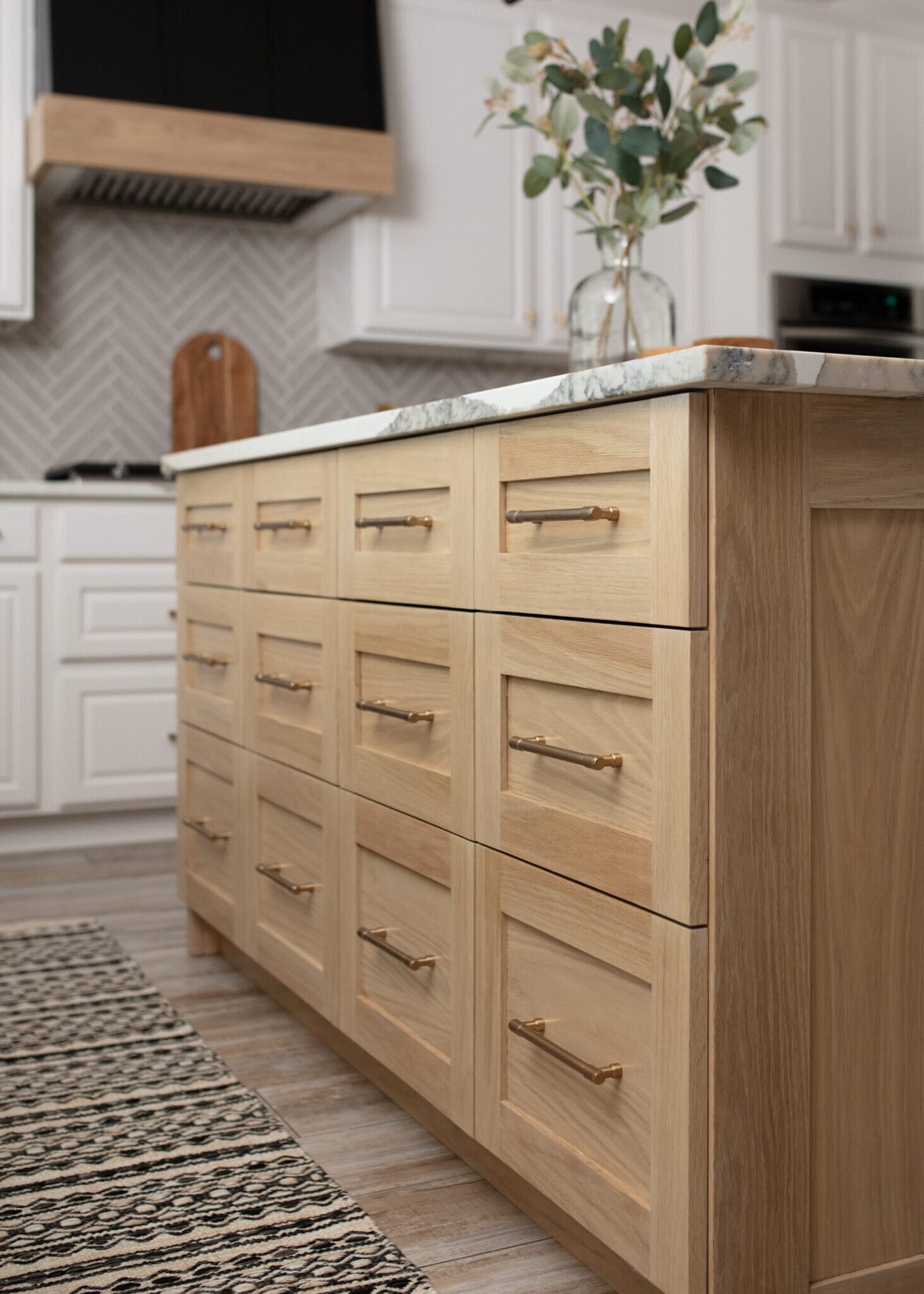 White oak island with deep drawers and brass pulls beside a patterned runner in the Ambrose Kitchen project by Jennifer Kizzee Design