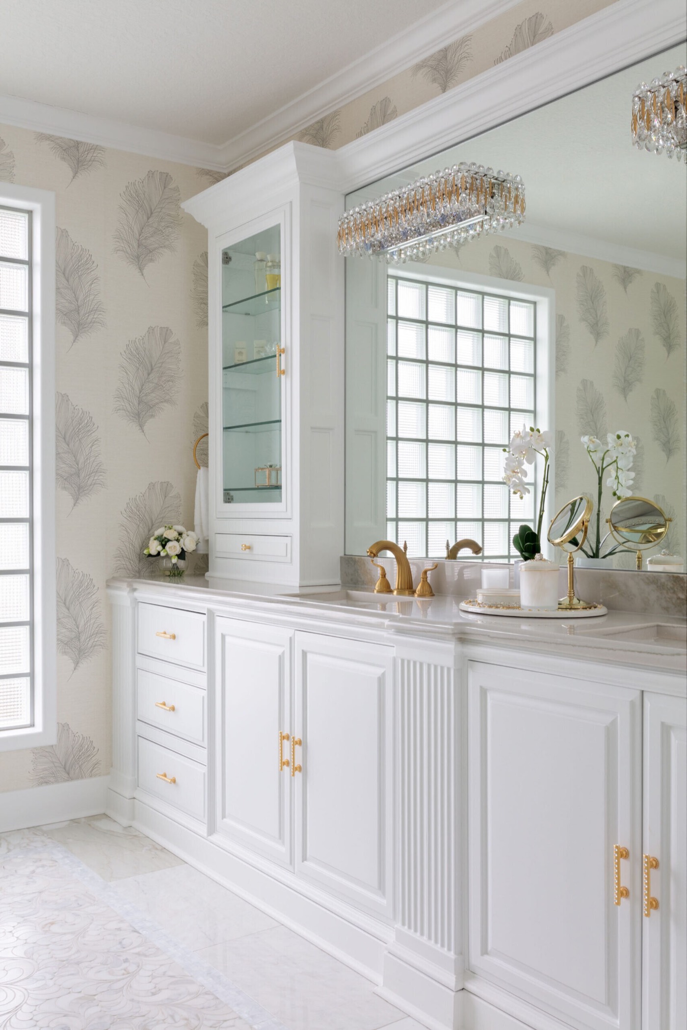 The white vanity run with a fluted center panel and satin brass bar pulls, its full-width mirror reflecting a glass block window in the Blue Heron Bathroom project by Jennifer Kizzee Design