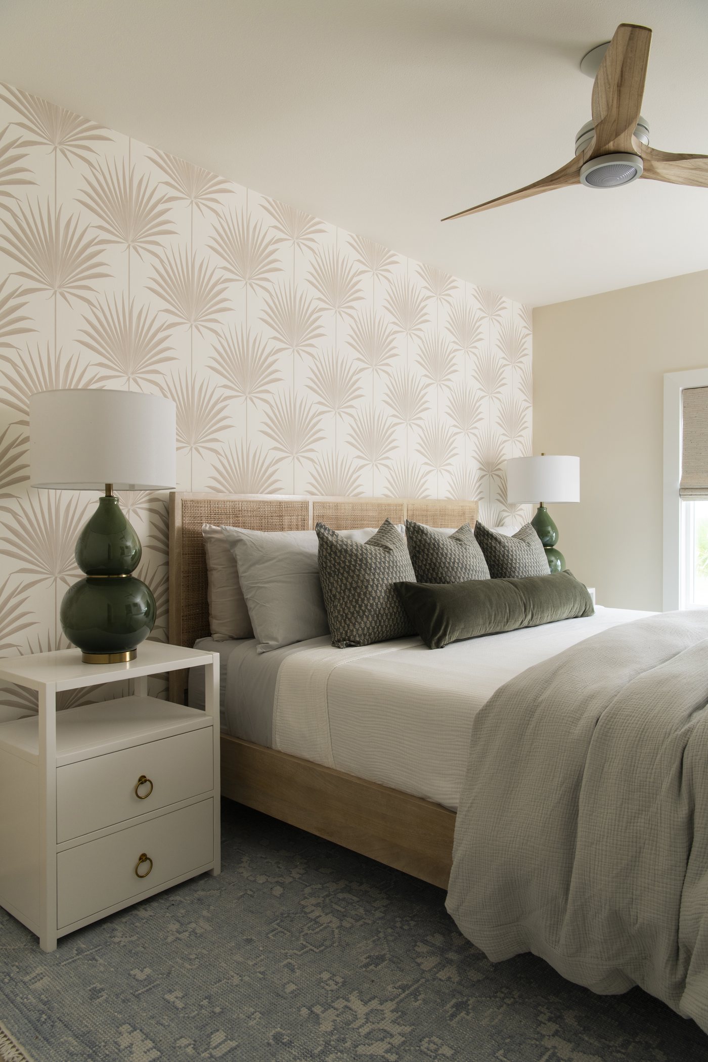 Bedroom with palm print wallpaper, an upholstered bed and white nightstands in the Bolivar Beach House project by Jennifer Kizzee Design