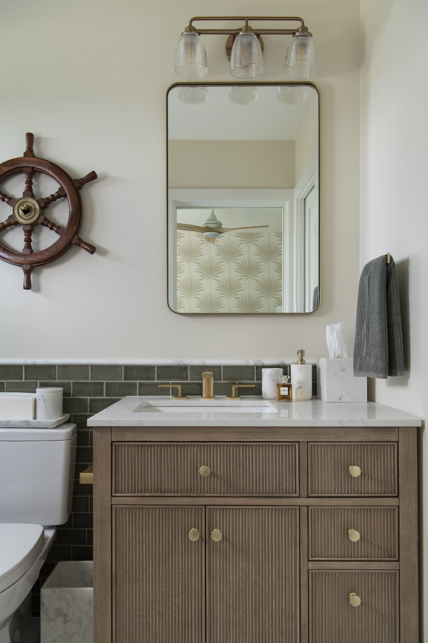 Fluted wood vanity with brass fittings, an arched mirror and green tile in the Bolivar Beach House project by Jennifer Kizzee Design
