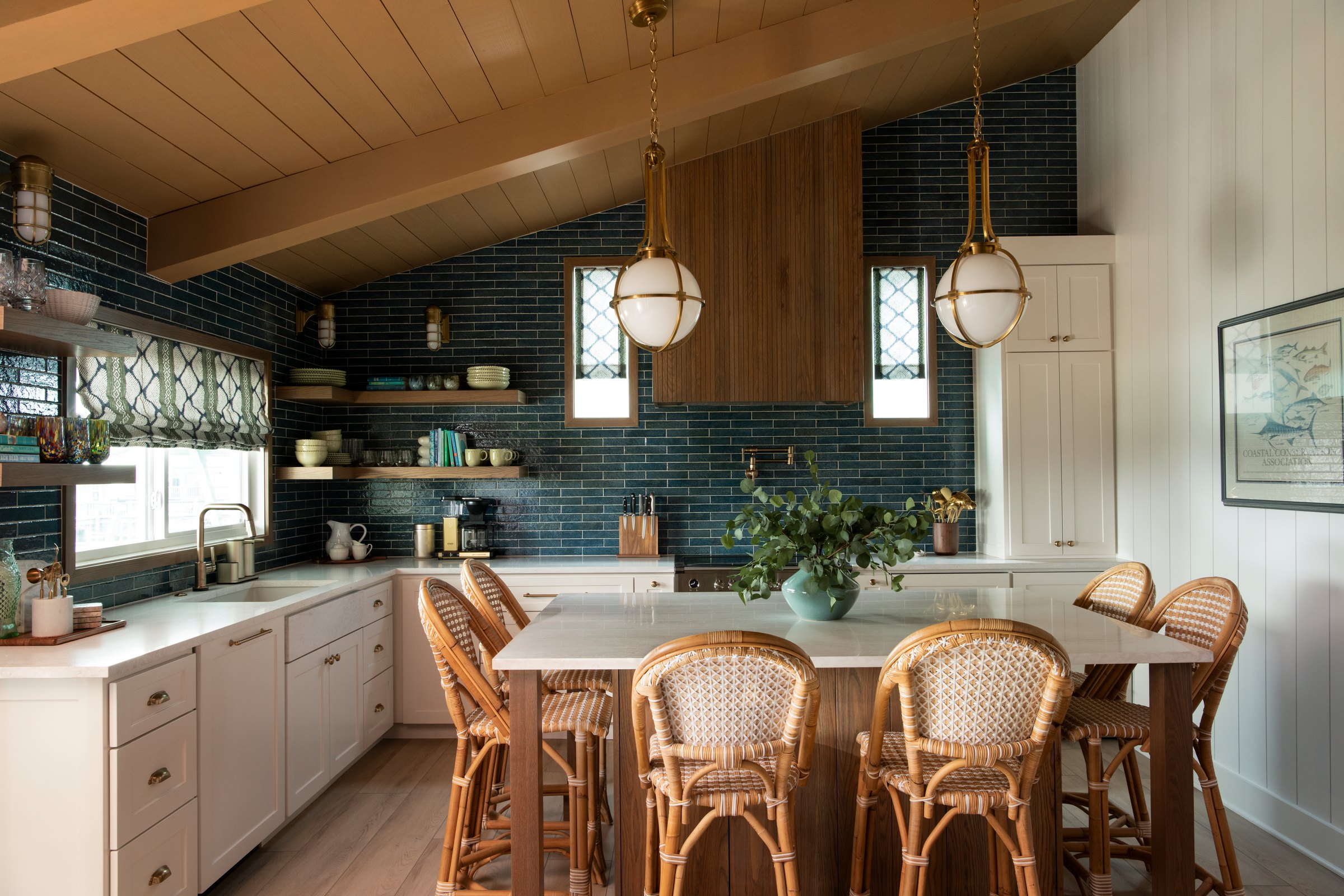 Kitchen with blue green tile to the ceiling, a white quartz island and rattan stools under brass globe pendants in the Bolivar Beach House project by Jennifer Kizzee Design