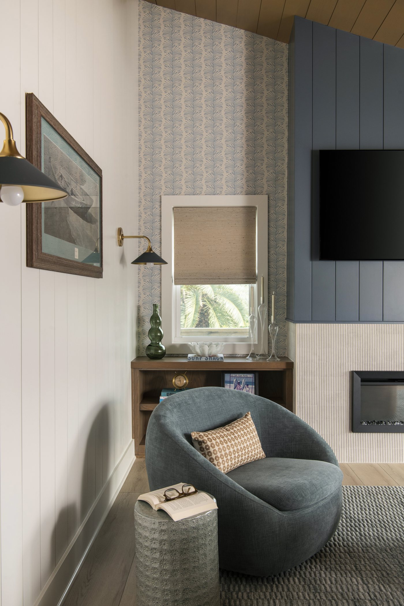 Living room corner with a teal swivel chair, a patterned ottoman and a built in desk beside the fireplace in the Bolivar Beach House project by Jennifer Kizzee Design