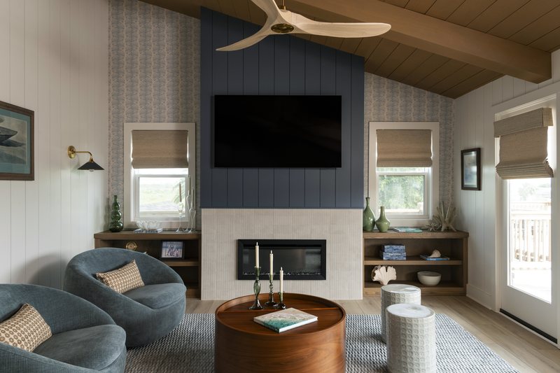 Living room with teal swivel chairs, a round walnut table and a plank ceiling following the roof line in the Bolivar Beach House project by Jennifer Kizzee Design