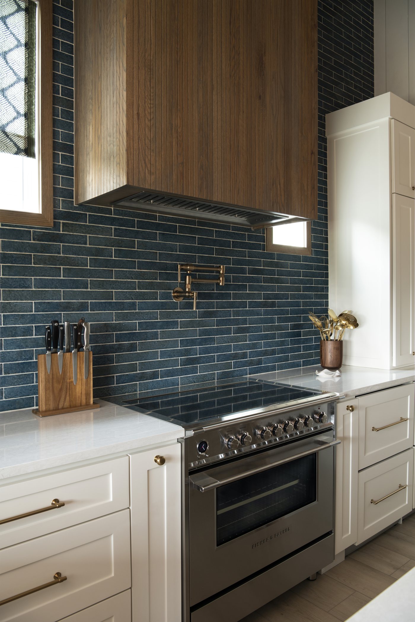 Range wall with a wood hood and blue green stacked tile behind a stainless range in the Bolivar Beach House project by Jennifer Kizzee Design