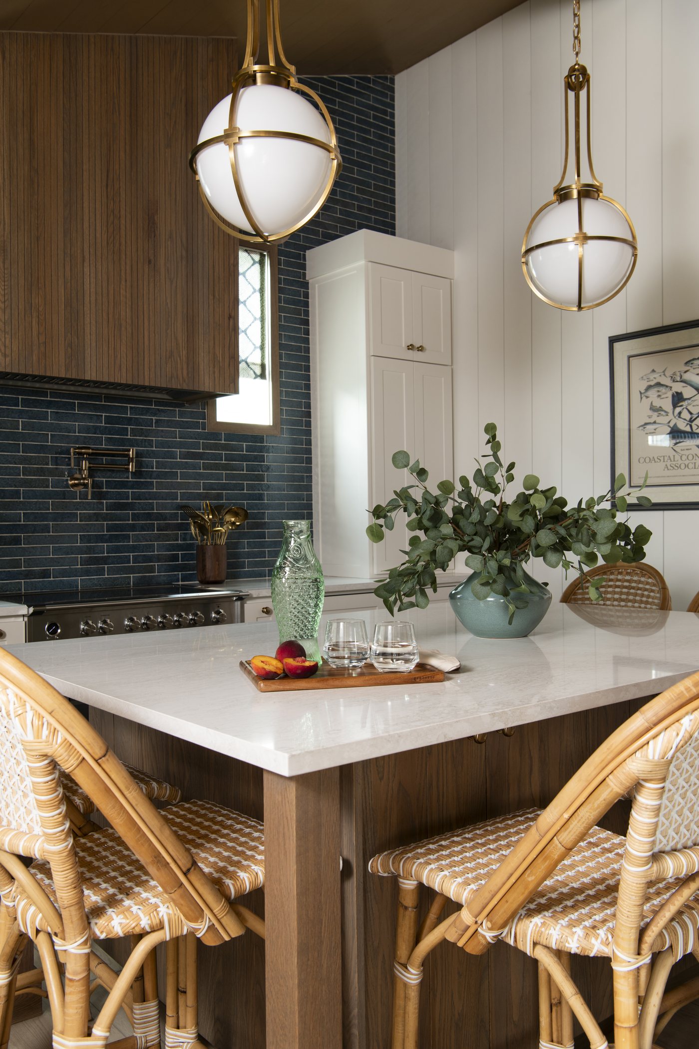 White quartz island on a walnut base with rattan stools and brass globe pendants in the Bolivar Beach House project by Jennifer Kizzee Design