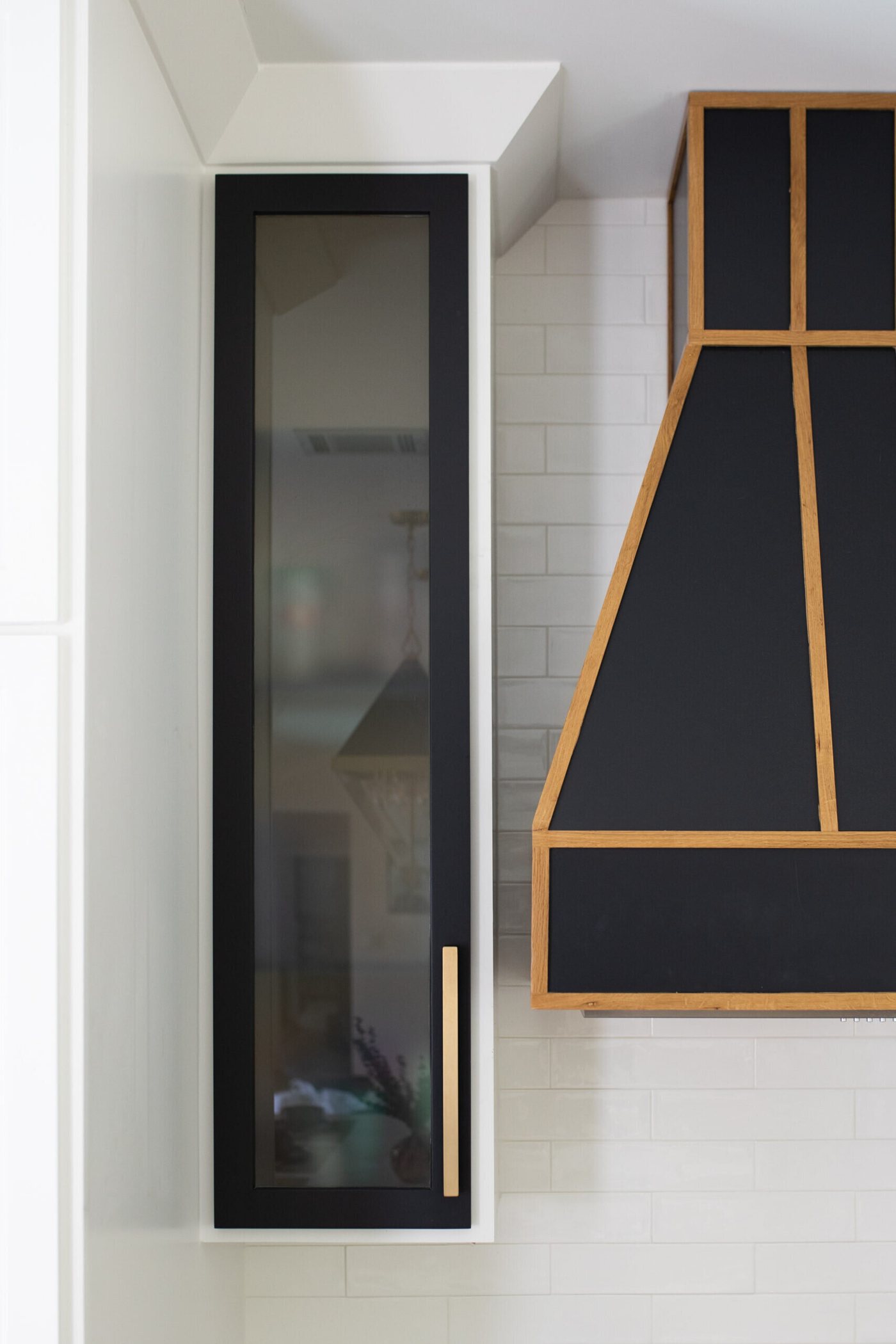 Black glass front cabinet with brass trim beside the hood in the Branstetter Kitchen project by Jennifer Kizzee Design