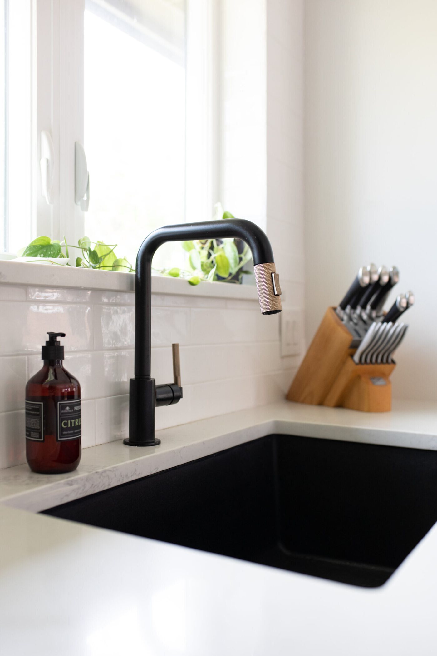 Black undermount sink with a black gooseneck faucet under a window in the Branstetter Kitchen project by Jennifer Kizzee Design