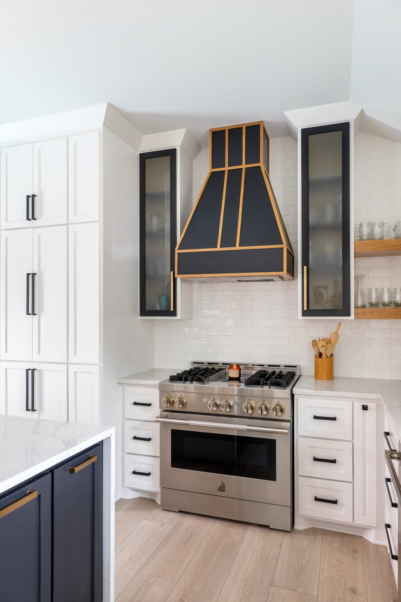 Range wall with white subway tile, stainless range and black glass cabinets in the Branstetter Kitchen project by Jennifer Kizzee Design