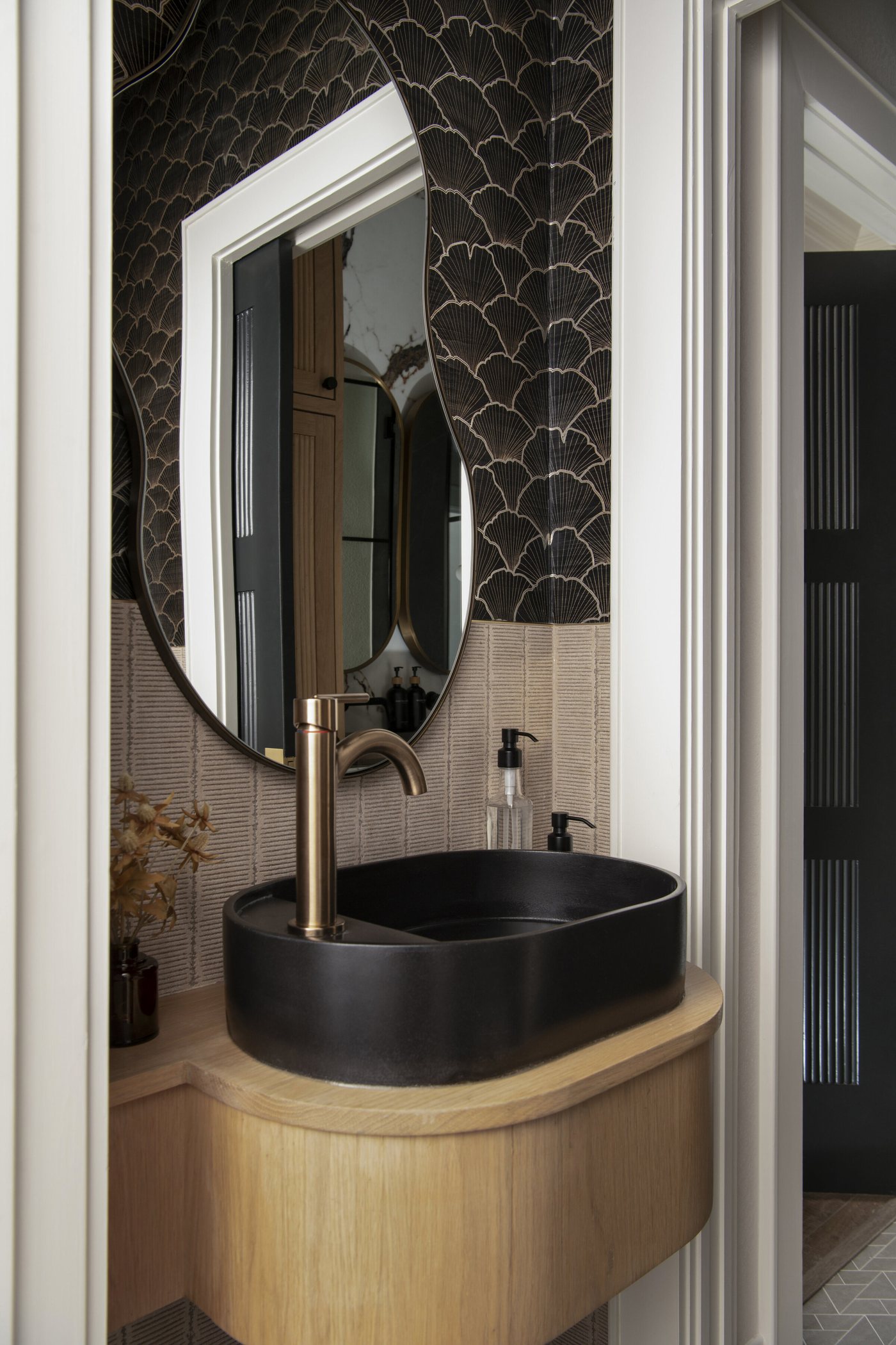Black stone vessel sink with a brass faucet under an oval mirror on scalloped tile in the Collective Washroom project by Jennifer Kizzee Design