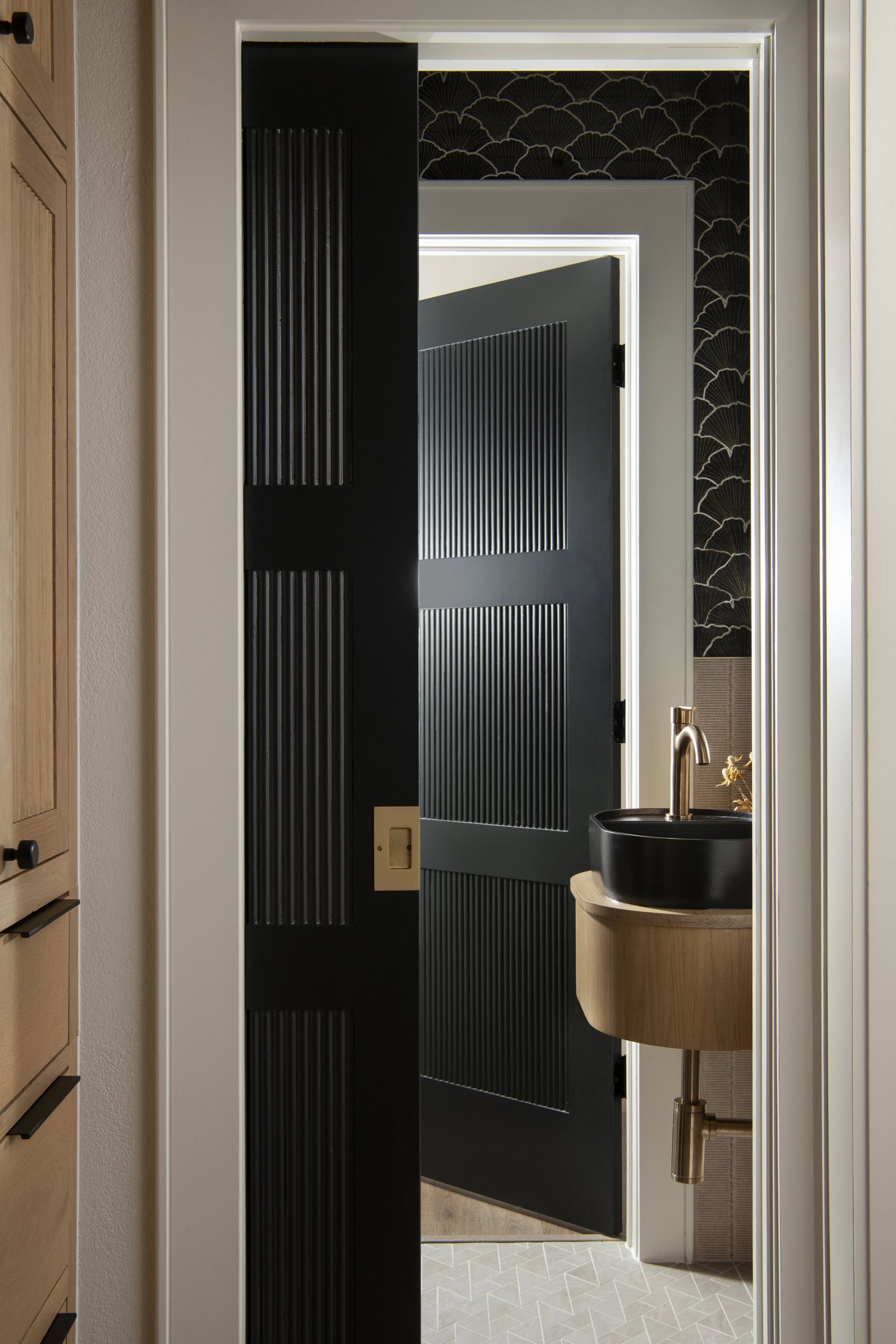 Fluted black door opening to the powder room with its brass faucet in the Collective Washroom project by Jennifer Kizzee Design