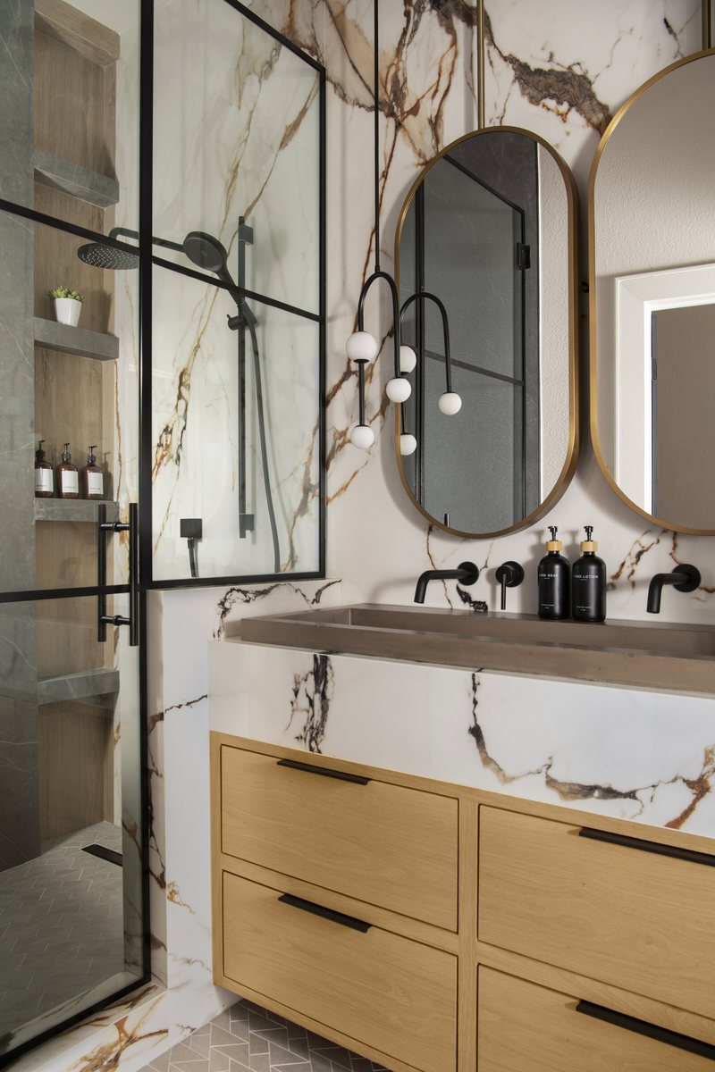 Marble slab wall behind oval mirrors above a white oak vanity in the Collective Washroom project by Jennifer Kizzee Design