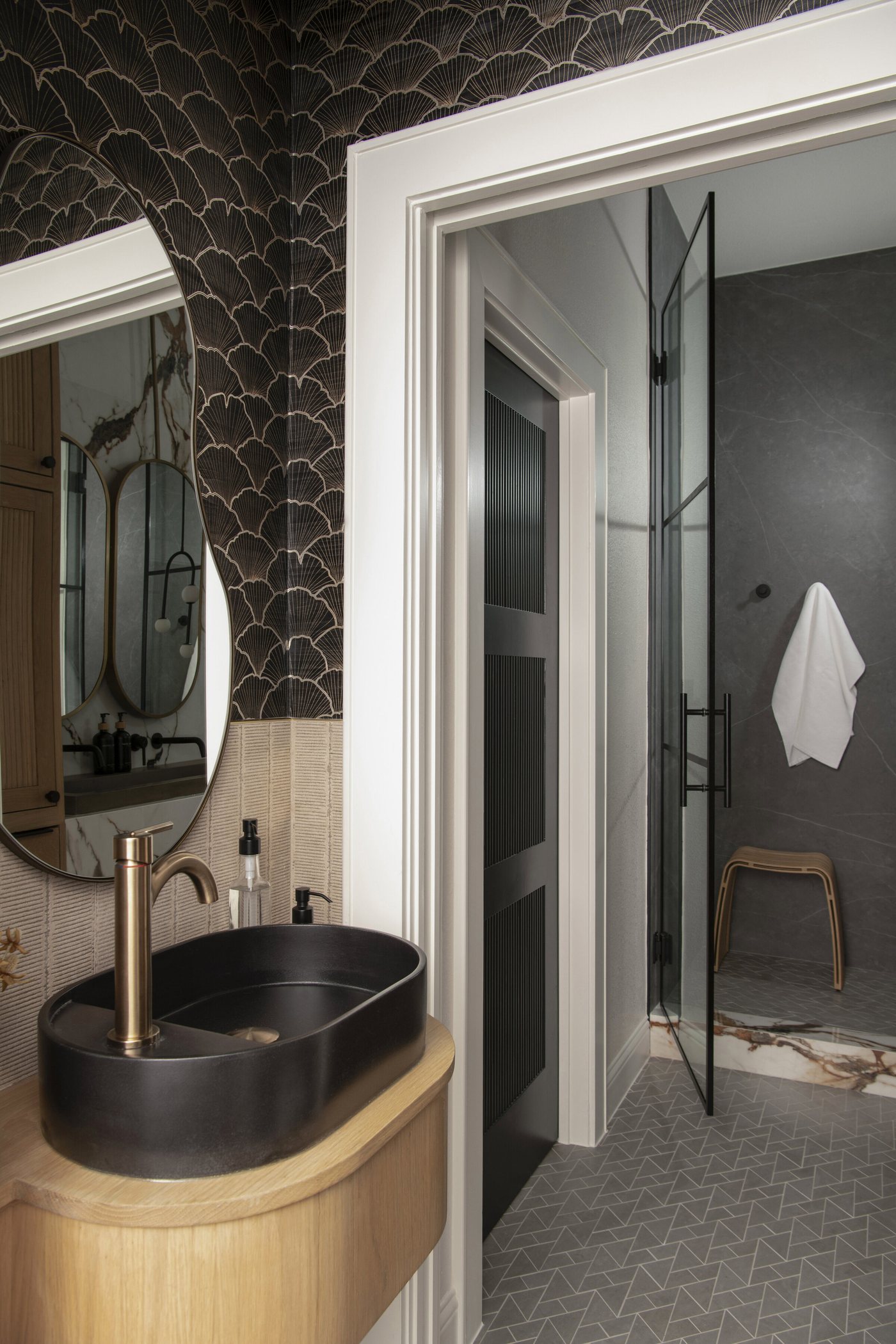 Powder room with a black stone vessel sink on a curved oak vanity, looking through to a shower in the Collective Washroom project by Jennifer Kizzee Design