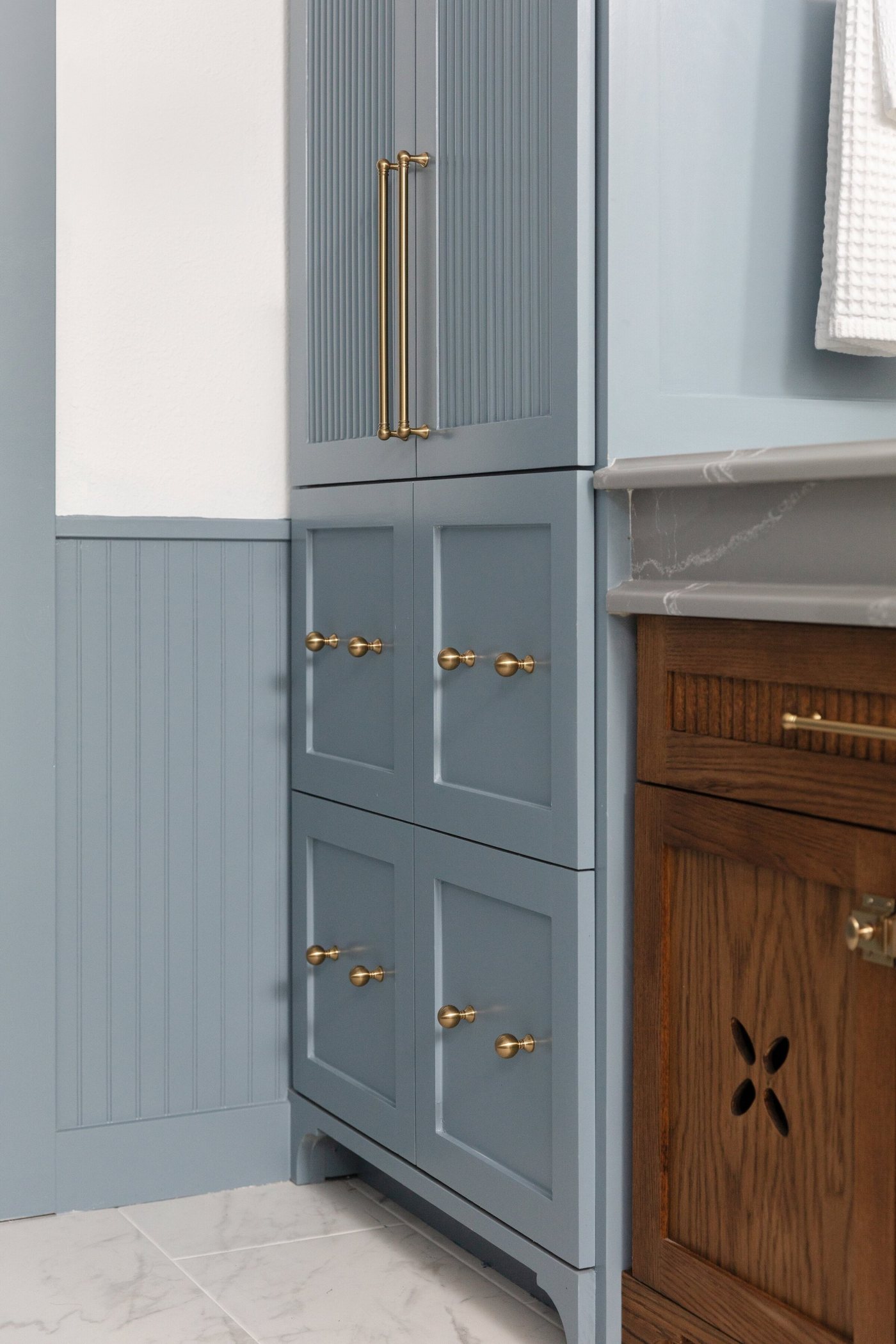 Blue beadboard storage tower beside the walnut vanity in the Crescent Bath project by Jennifer Kizzee Design