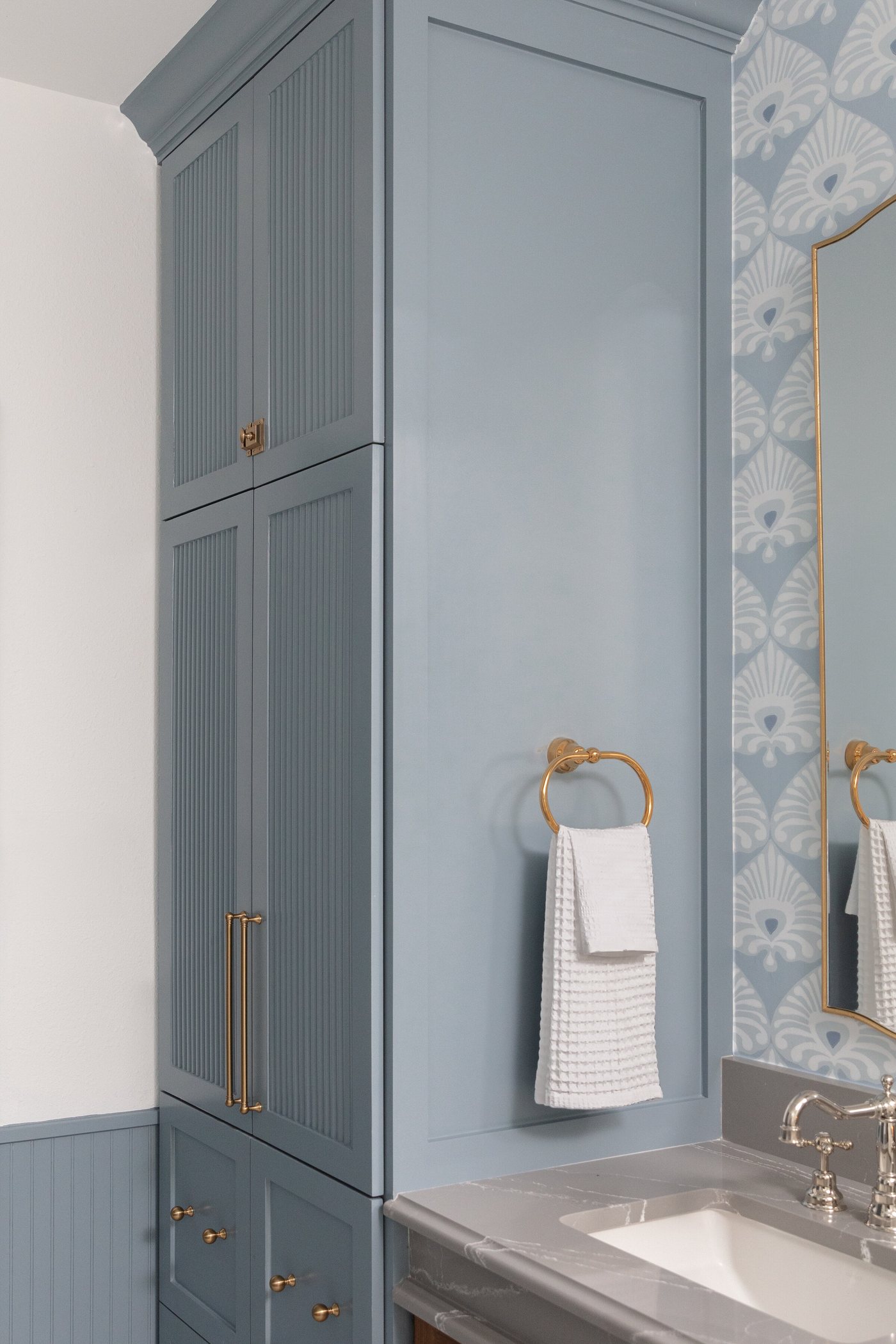 Blue cabinetry and counter with a towel ring and gilt mirror in the Crescent Bath project by Jennifer Kizzee Design