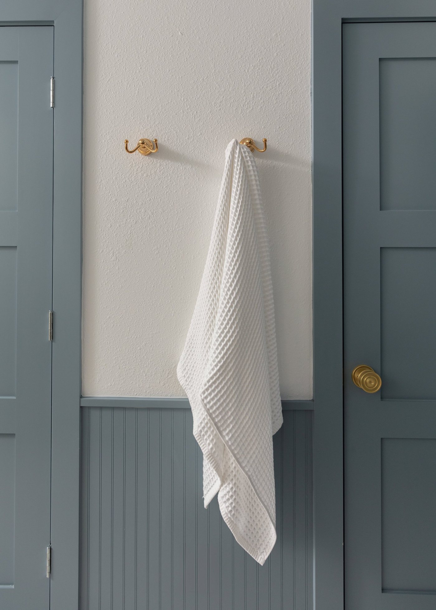 Blue paneled door and beadboard wall with brass hooks and a waffle towel in the Crescent Bath project by Jennifer Kizzee Design