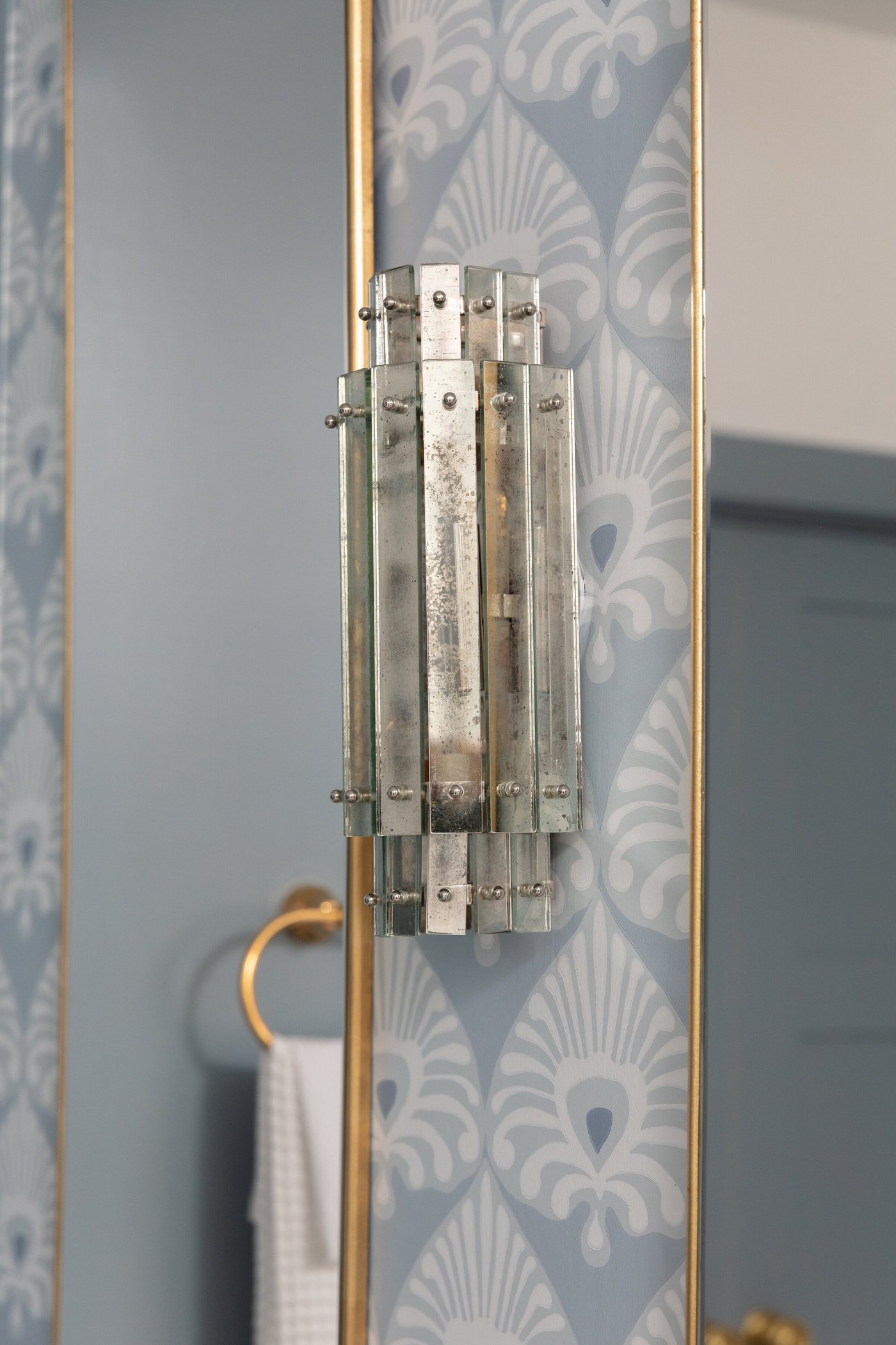 Glass and brass sconce mounted on the patterned wallpaper in the Crescent Bath project by Jennifer Kizzee Design