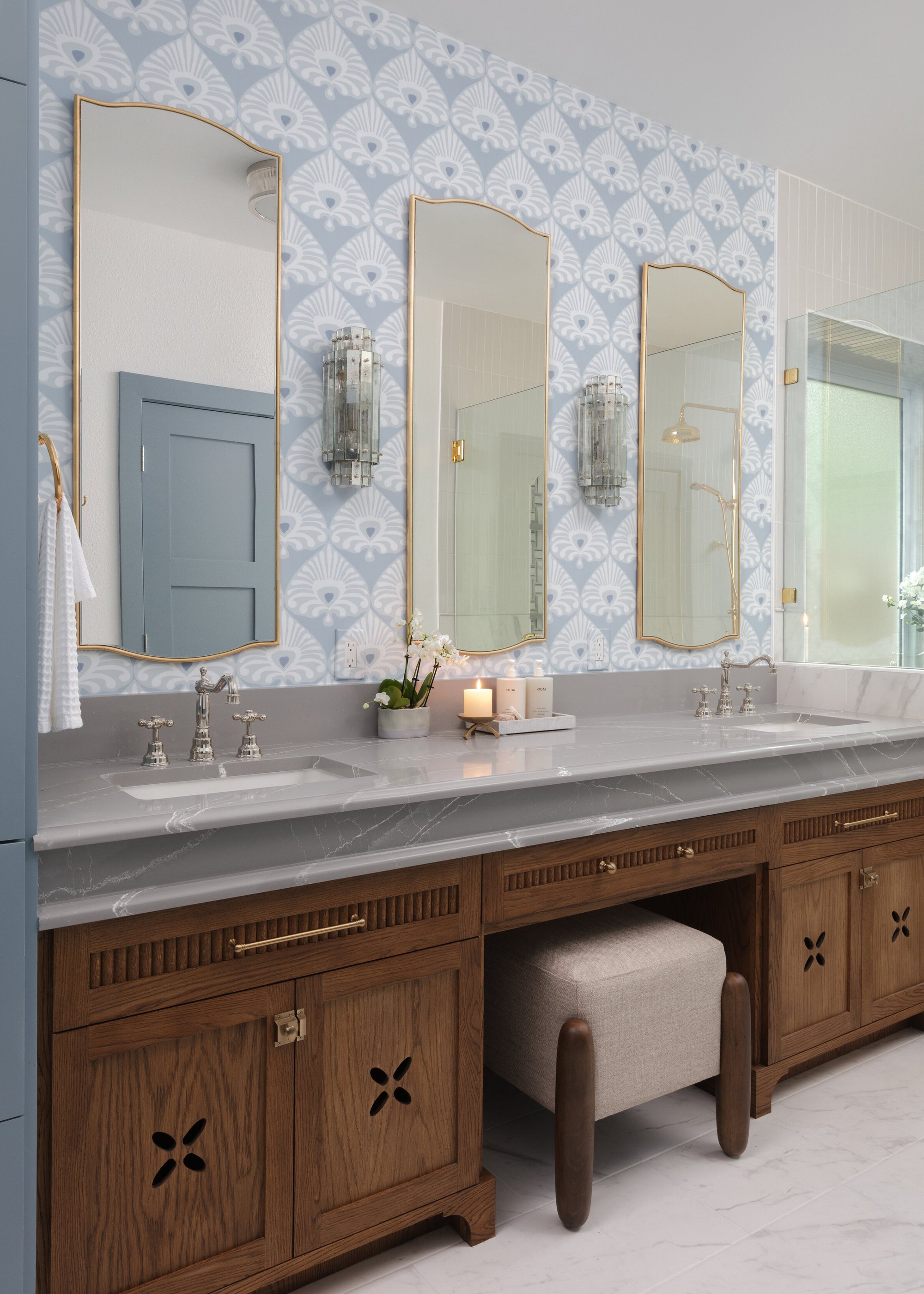 Primary bath with blue patterned wallpaper, a carved walnut double vanity and arched mirrors in the Crescent Bath project by Jennifer Kizzee Design