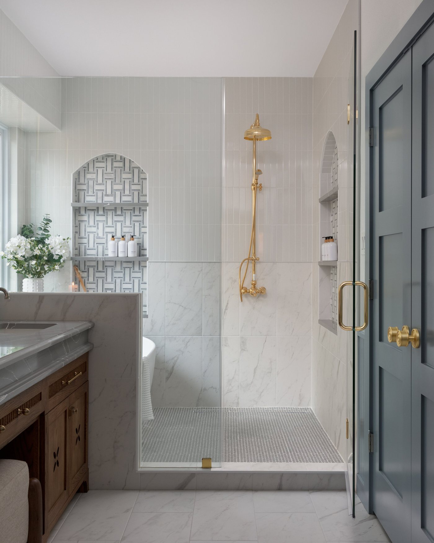 Walk-in shower with brass fittings behind a glass door in the Crescent Bath project by Jennifer Kizzee Design