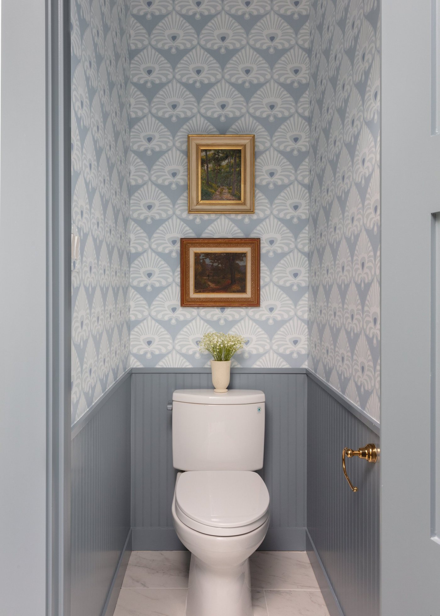Water closet with blue patterned wallpaper, beadboard wainscot and framed art in the Crescent Bath project by Jennifer Kizzee Design