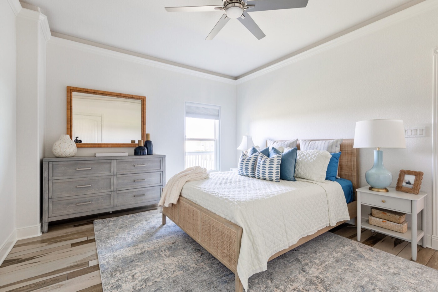 Bedroom with a woven panel bed, a gray washed dresser, and a rattan-framed mirror in the Crystal Beach Vacation Home project by Jennifer Kizzee Design