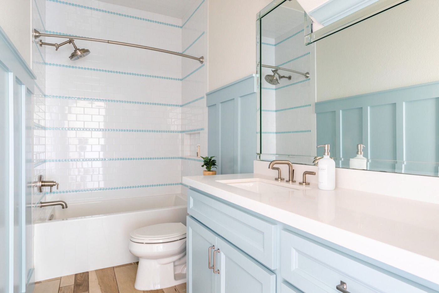 Hall bath with a tub and shower in white subway tile striped with aqua liner and pale blue board and batten walls in the Crystal Beach Vacation Home project by Jennifer Kizzee Design