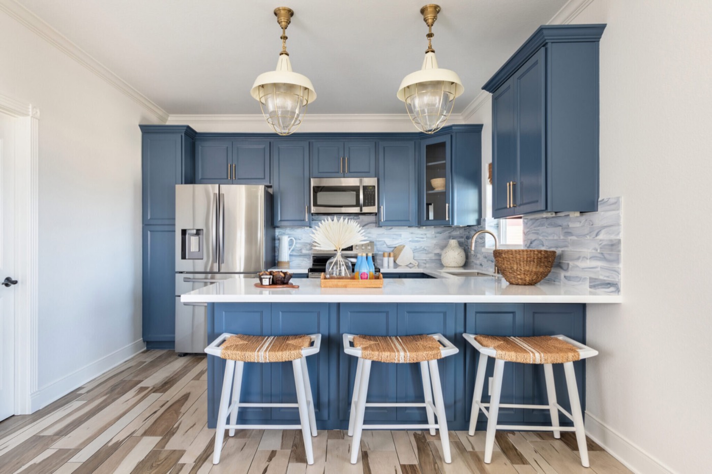 Kitchen peninsula with three woven seagrass stools under a pair of glass and brass pendants in the Crystal Beach Vacation Home project by Jennifer Kizzee Design