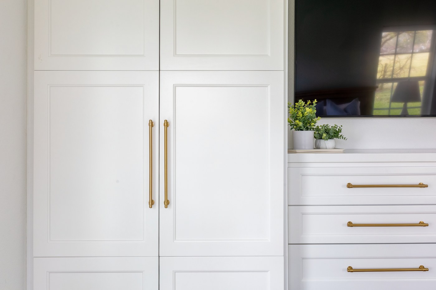Built-in white dresser bank and tall storage cabinet fitted with long brass bar pulls in the Emma Lane Guest House project by Jennifer Kizzee Design