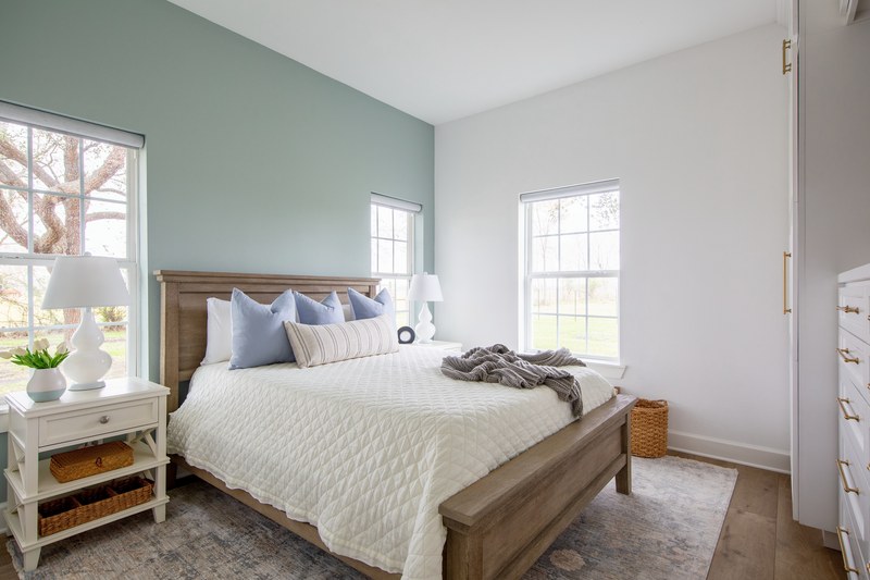Bedroom with a weathered oak panel bed centered on a sage green accent wall in the Emma Lane Guest House project by Jennifer Kizzee Design