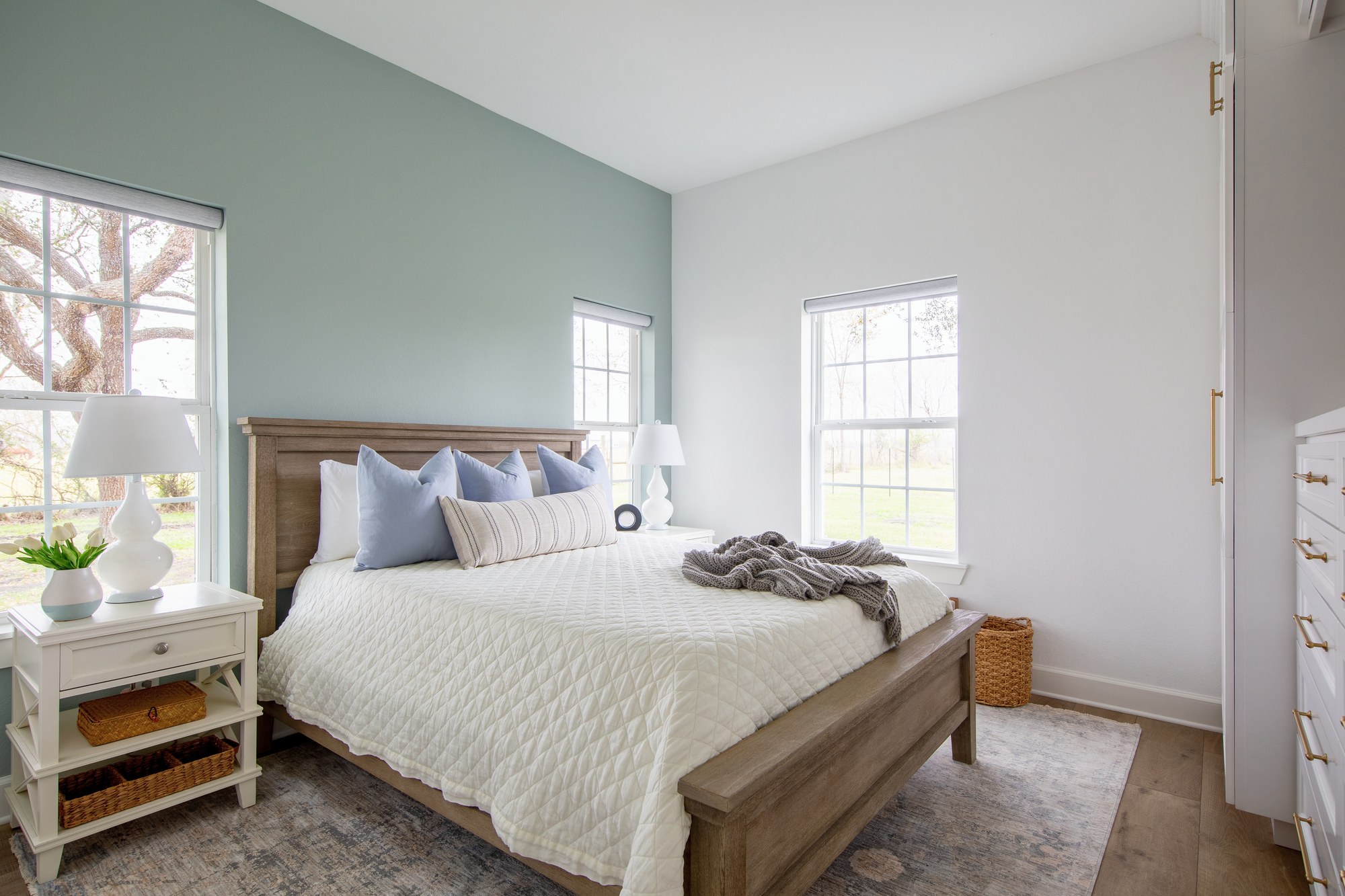 Bedroom with a weathered oak panel bed centered on a sage green accent wall in the Emma Lane Guest House project by Jennifer Kizzee Design