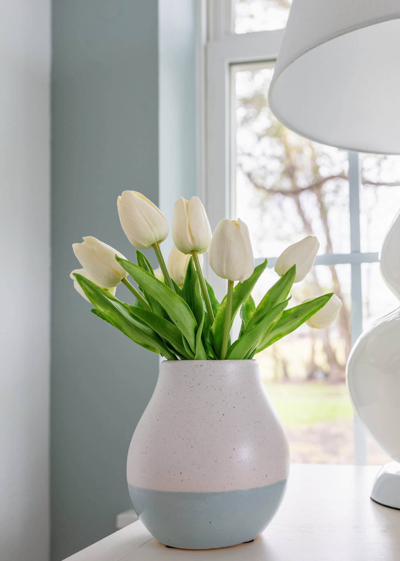 White tulips in a two-tone ceramic vase on the bedside table in the Emma Lane Guest House project by Jennifer Kizzee Design