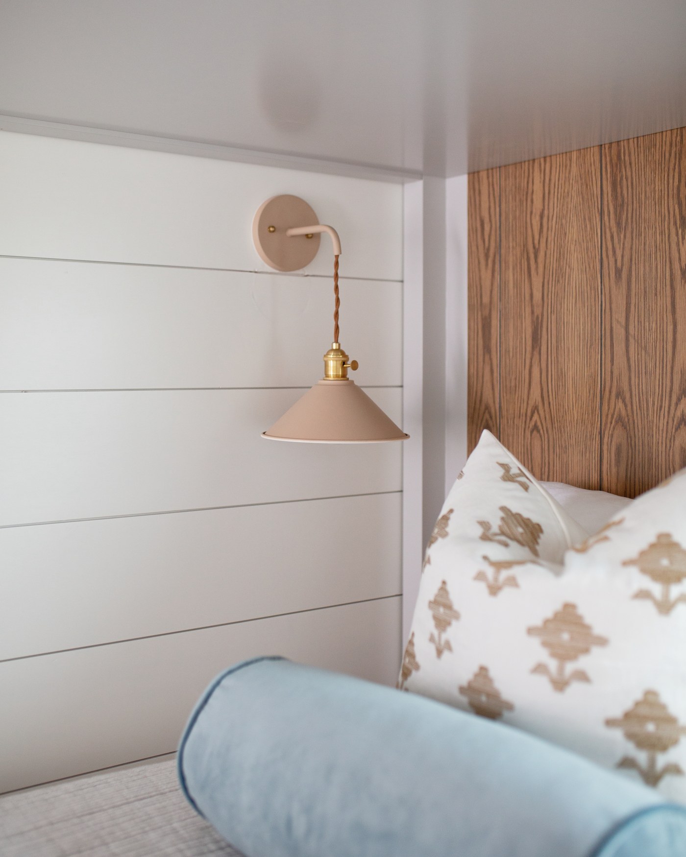 Brass swing-arm sconce on white shiplap above a teal velvet bolster in the Emma Lane Guest House project by Jennifer Kizzee Design