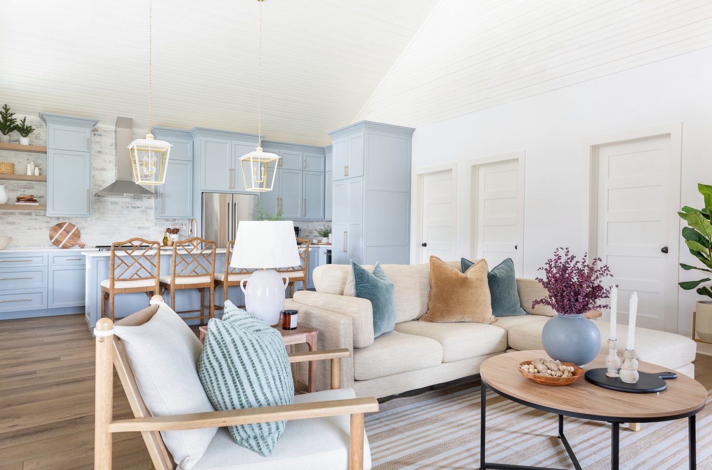 Open great room where an oatmeal sectional faces a powder blue kitchen under a vaulted white plank ceiling in the Emma Lane Guest House project by Jennifer Kizzee Design