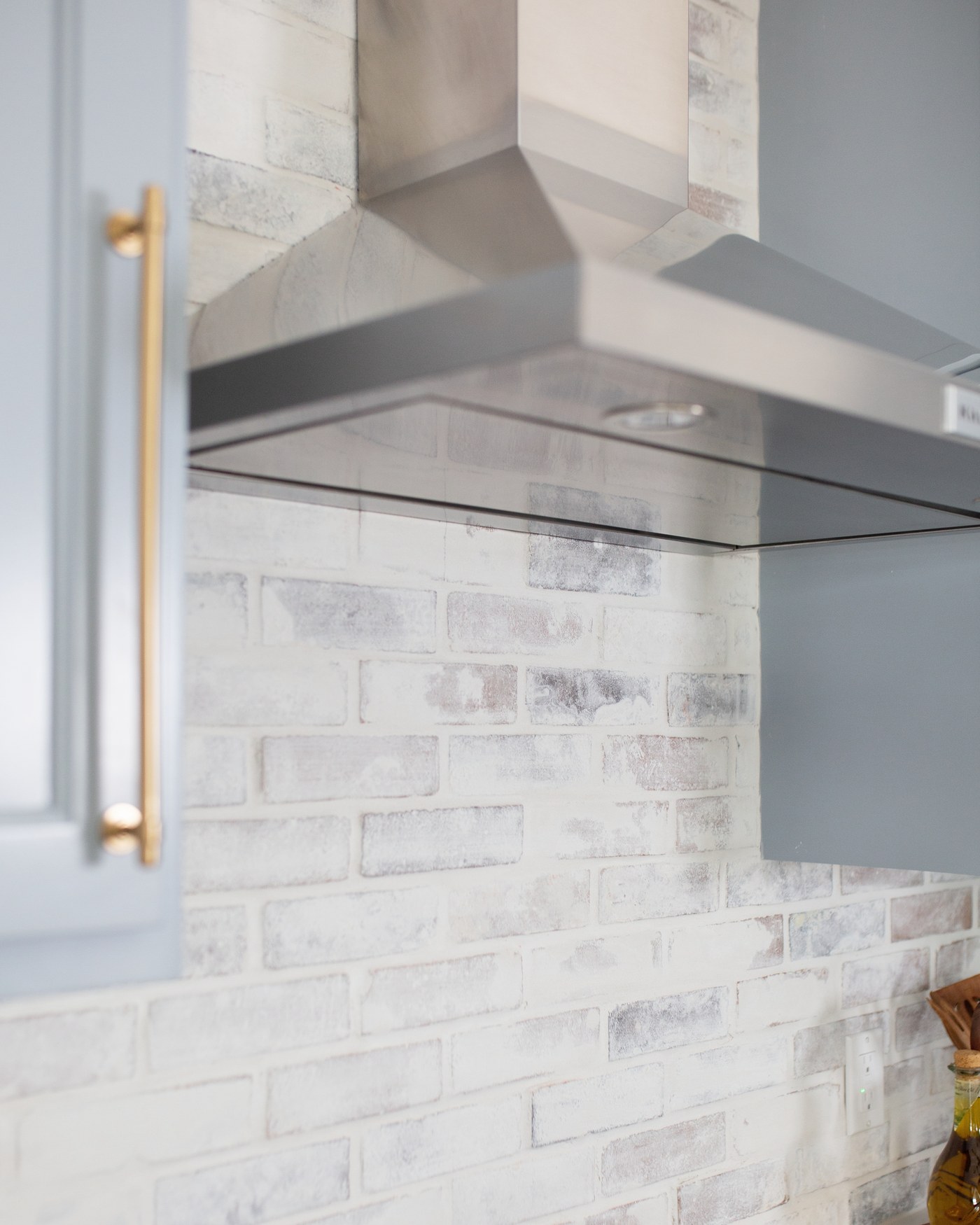 Stainless chimney hood set against a whitewashed thin brick backsplash in the Emma Lane Guest House project by Jennifer Kizzee Design