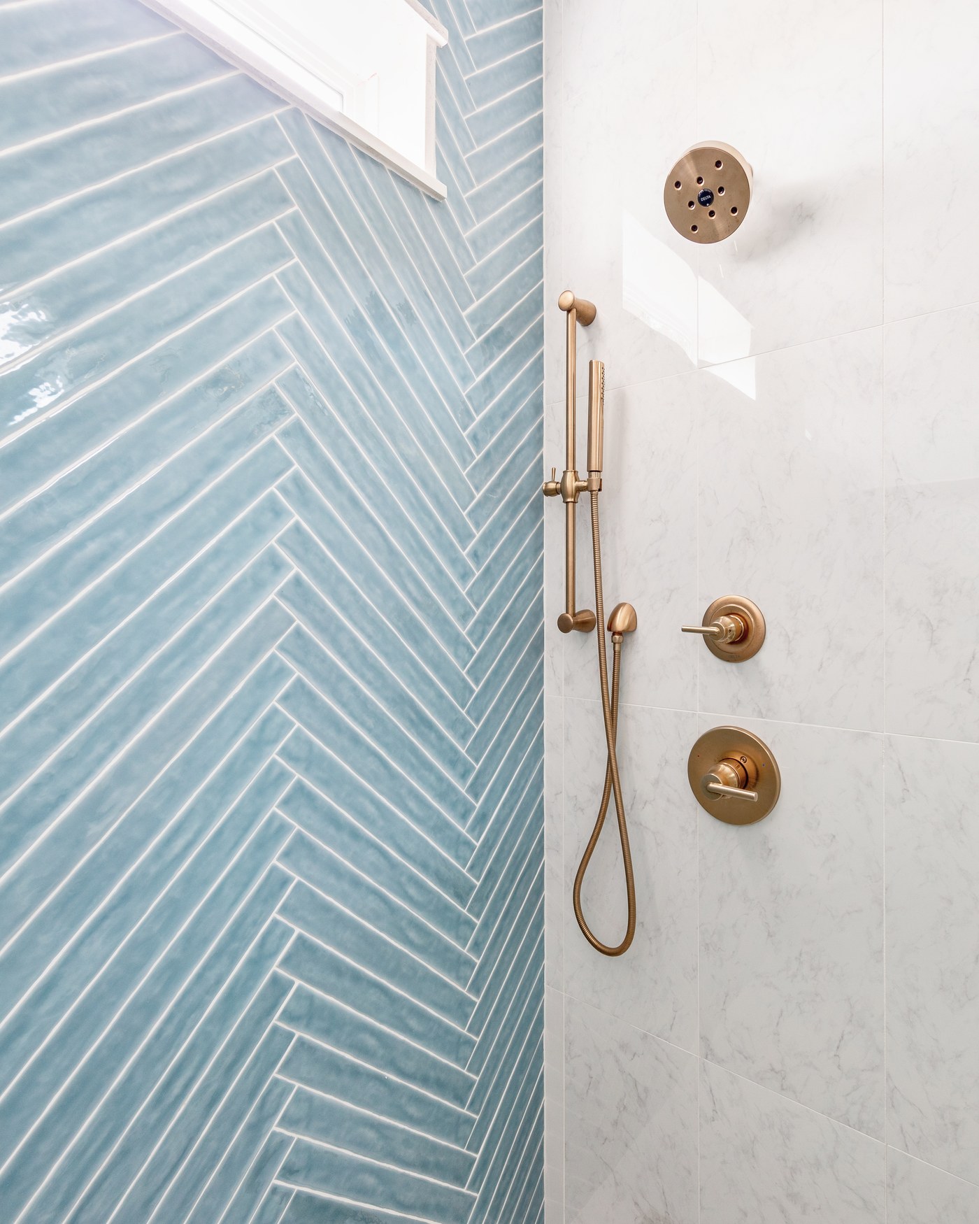 Brass shower head and hand shower on a slide bar against light blue herringbone tile in the Emma Lane Guest House project by Jennifer Kizzee Design