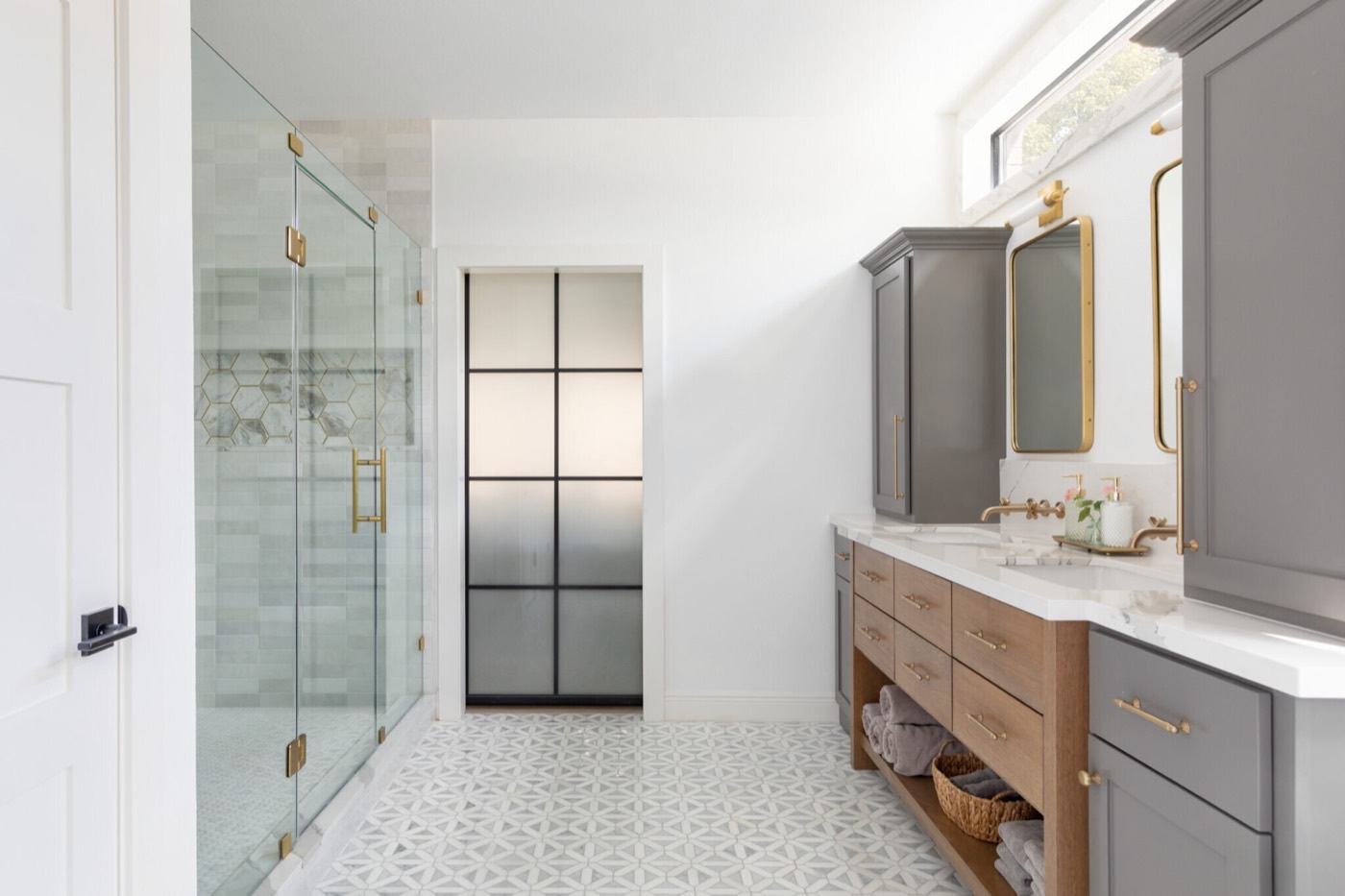Marble mosaic floor running between the glass shower and the vanity past a black steel frosted glass door in the Evergreen Suite Bathroom project by Jennifer Kizzee Design