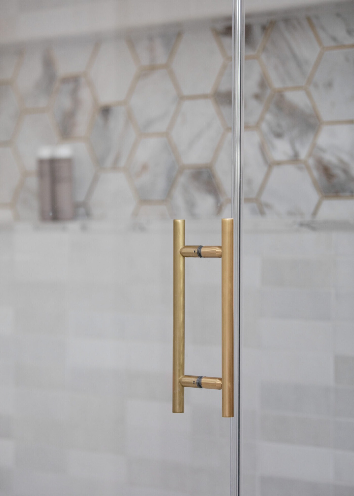 Brass shower door pull in front of a calacatta marble hexagon accent band in the Evergreen Suite Bathroom project by Jennifer Kizzee Design