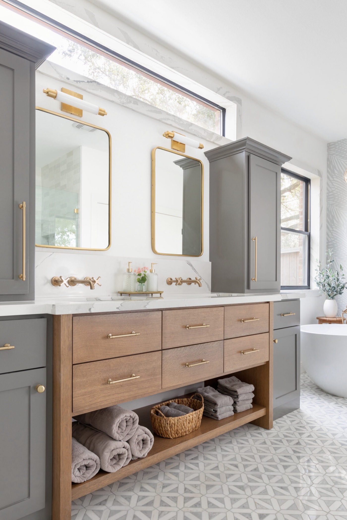 Brass wall-mount faucets with clover handles against a white marble slab backsplash in the Evergreen Suite Bathroom project by Jennifer Kizzee Design