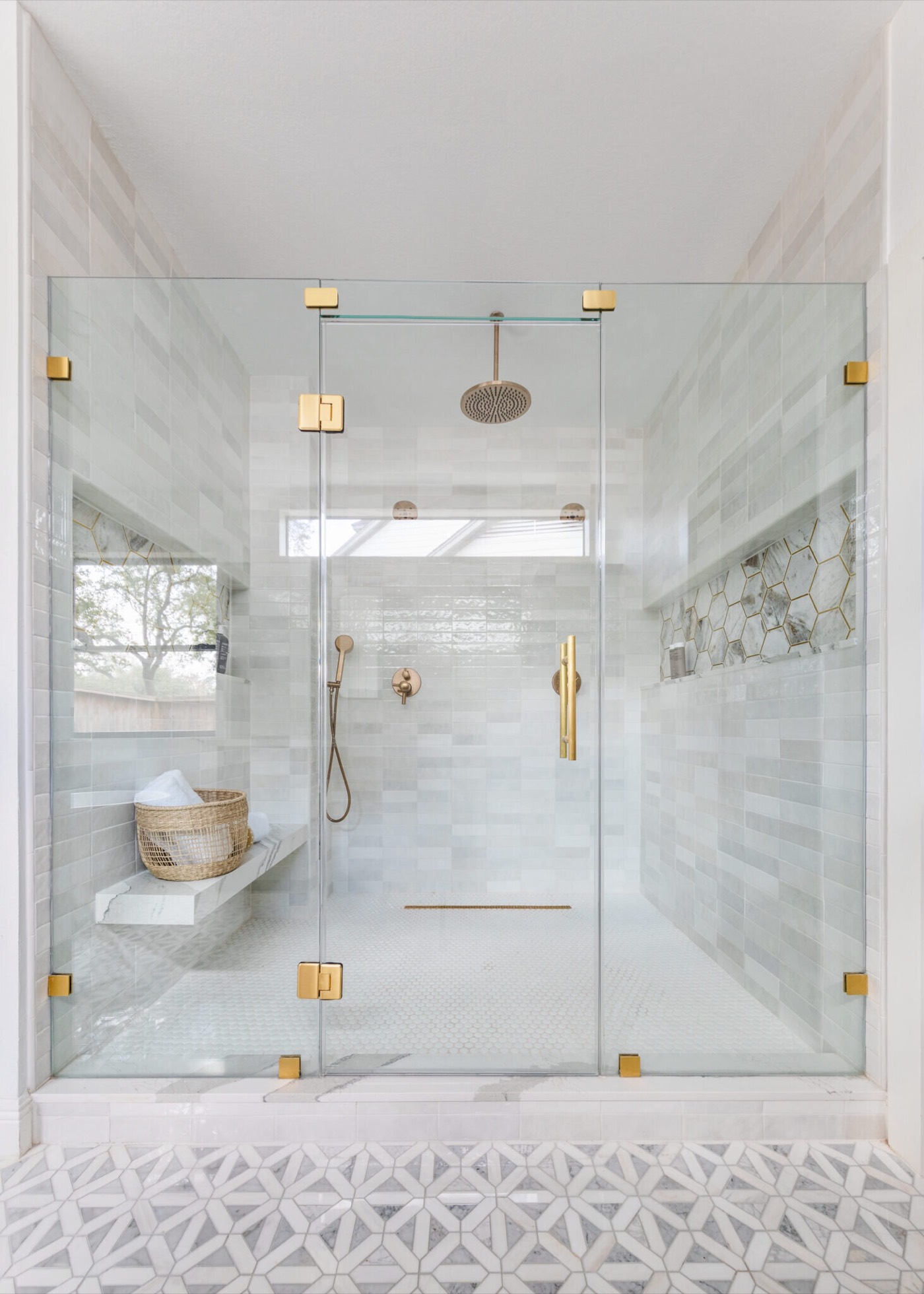 Frameless glass shower with brass hardware, a corner bench and a marble hexagon niche in the Evergreen Suite Bathroom project by Jennifer Kizzee Design