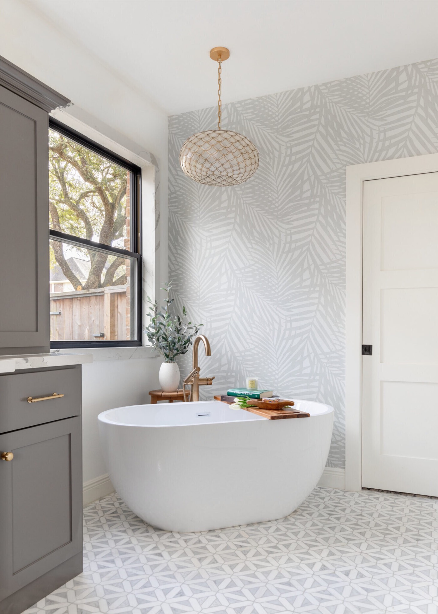 Freestanding oval tub beneath a capiz shell pendant on sage green palm wallpaper in the Evergreen Suite Bathroom project by Jennifer Kizzee Design